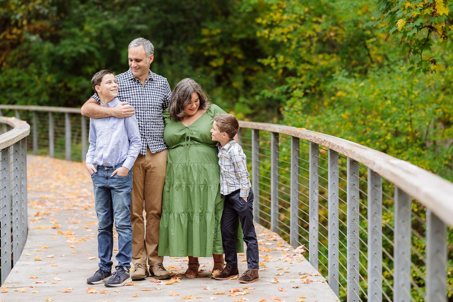 Family of five posing on a wooden bridge surrounded by autumn foliage during an outdoor fall photo session.