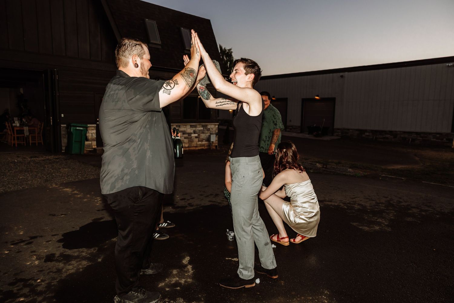 Three people giving high-fives outside at dusk during a wedding celebration.