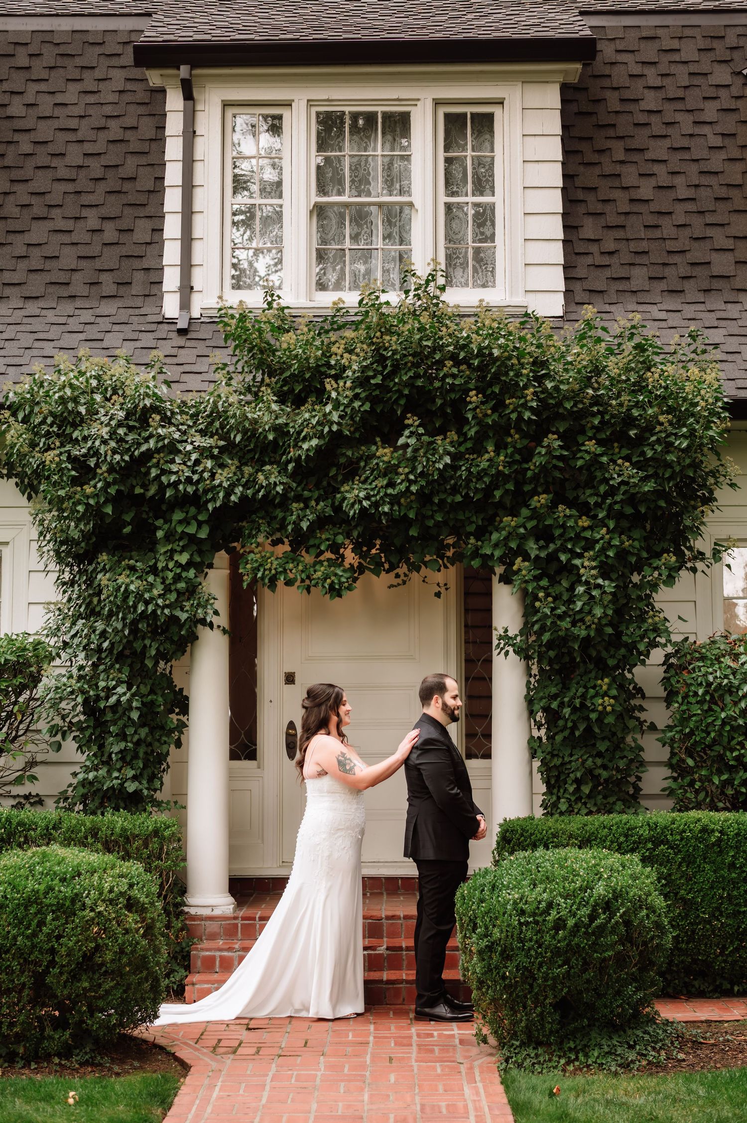 Bride and groom sharing first look moment outside ivy-covered white estate home.