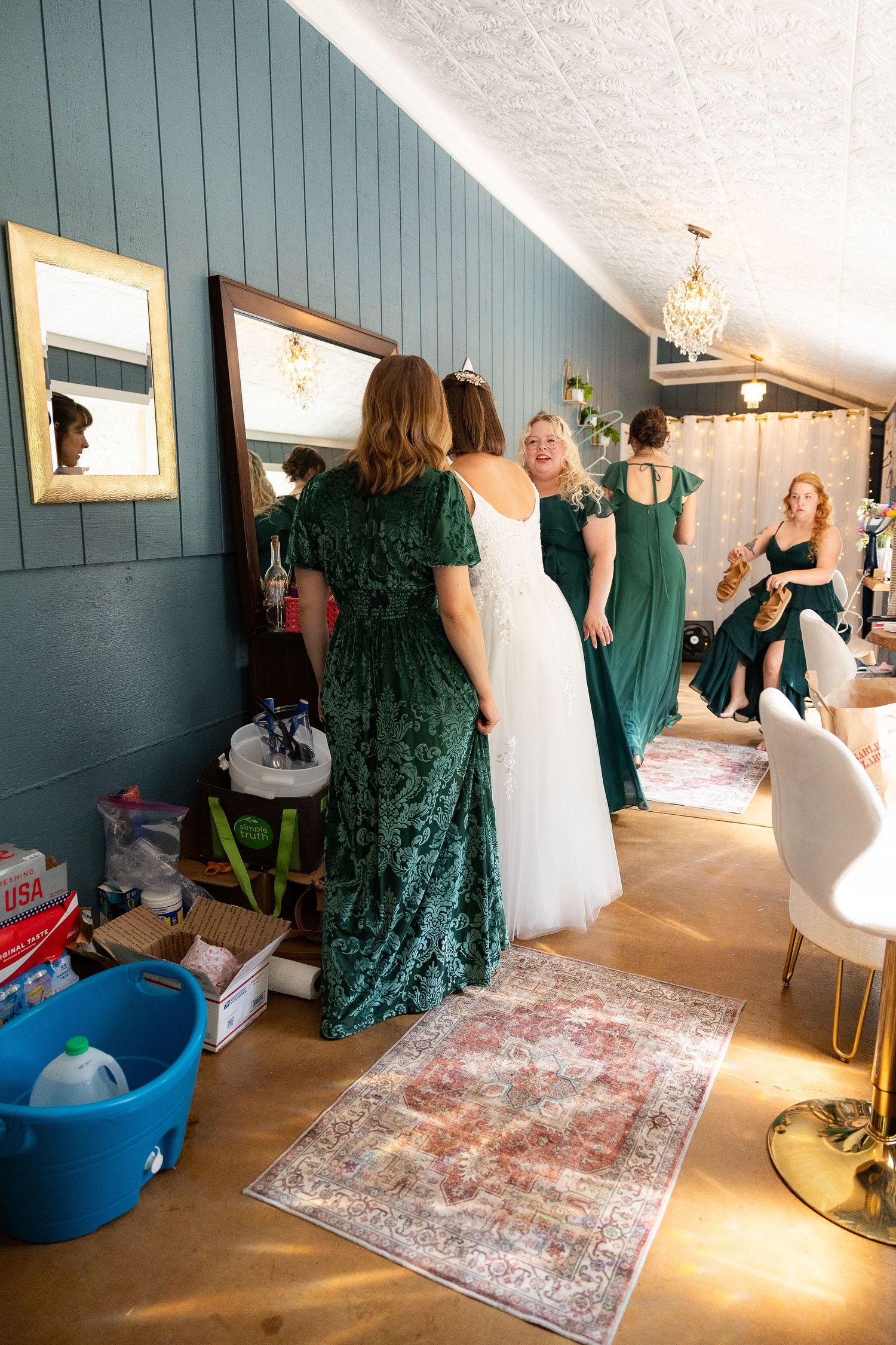Bride in white gown with bridesmaids in green velvet dresses getting ready in a bridal suite.
