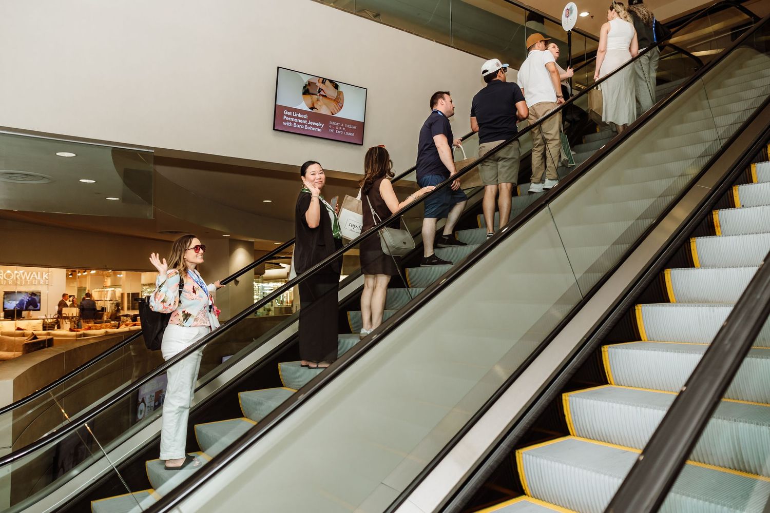 Conference attendees riding escalators inside bright modern convention center during professional event.
