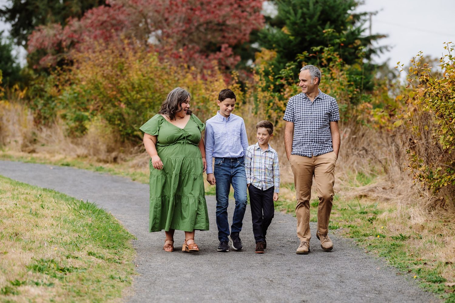 Family of four walking on a path surrounded by colorful autumn foliage during an outdoor photo session.