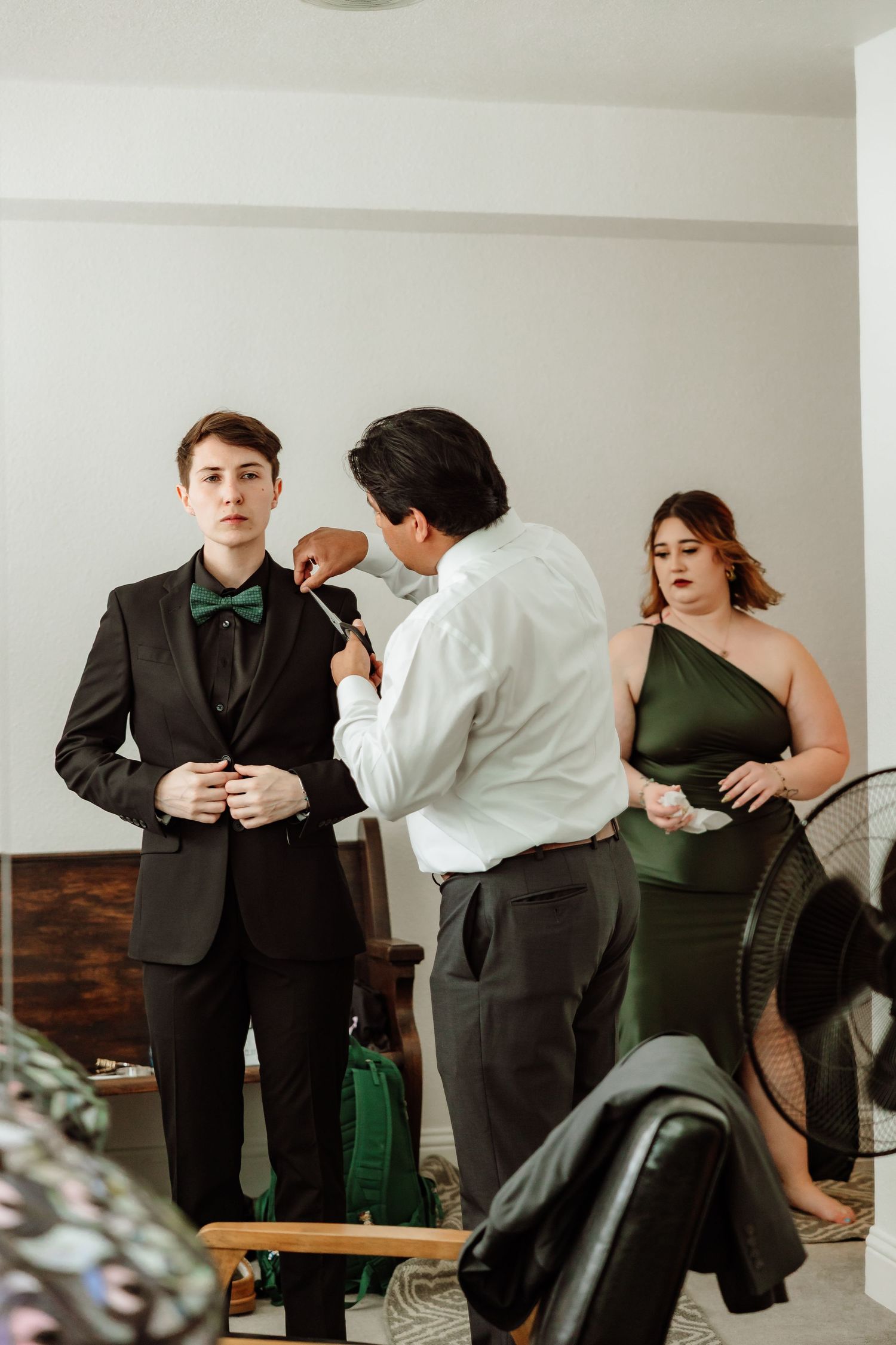 Wedding party helps young groom in black tuxedo with green bow tie with final preparations.