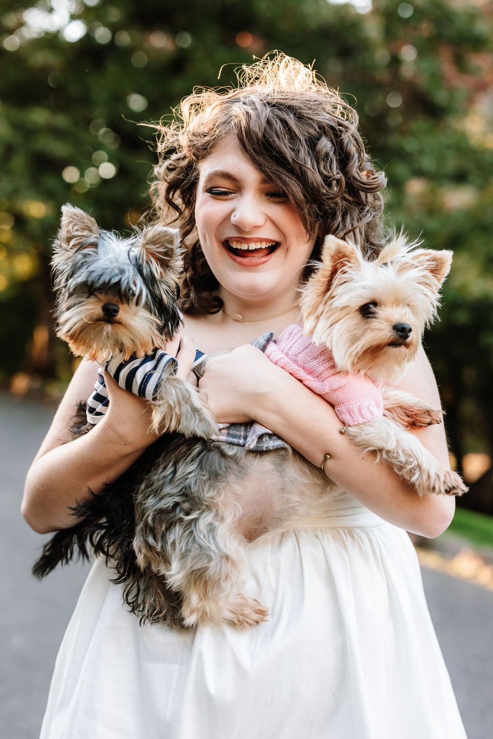 High school senior girl laughing while holding two Yorkshire Terrier dogs outdoors in Portland