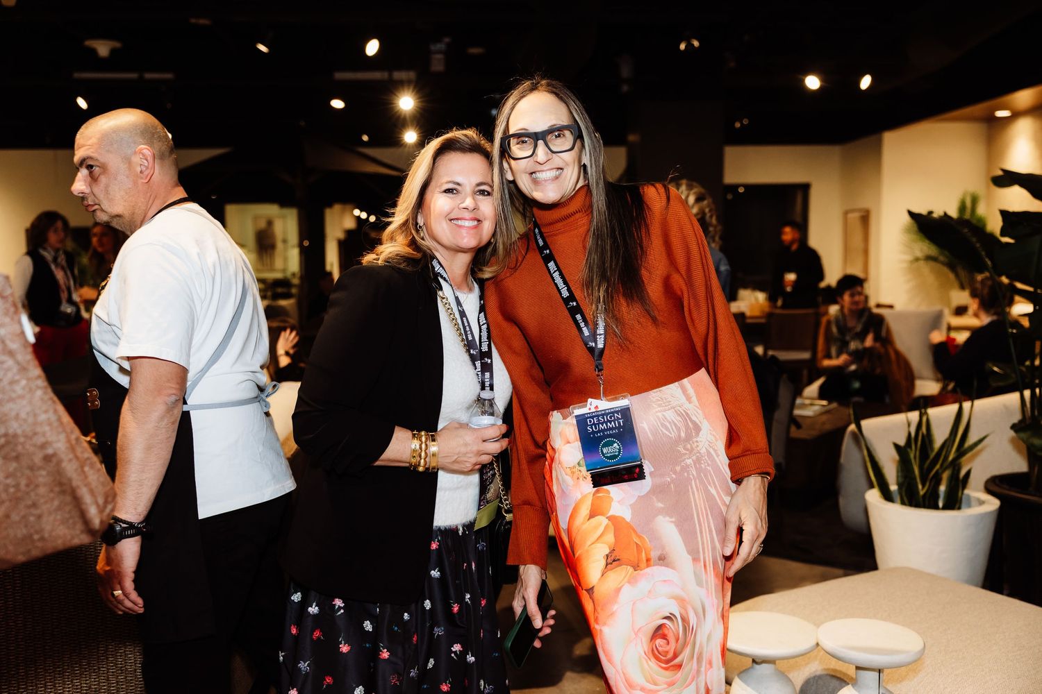 Two women smiling and posing together at a professional networking event wearing lanyards.