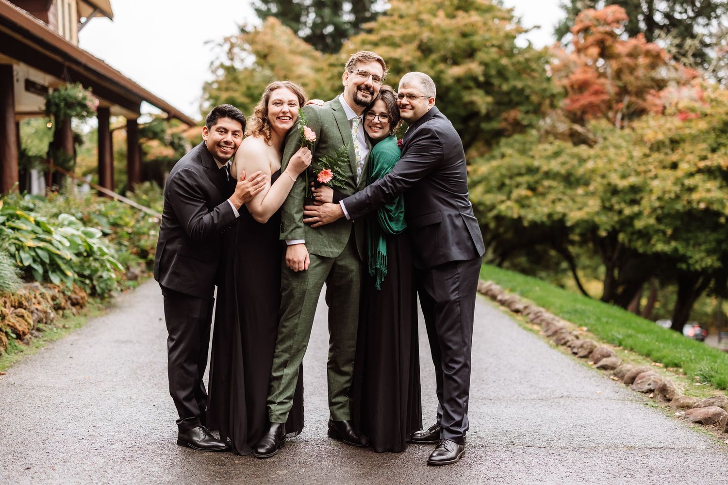 Happy wedding party group of five posing and hugging on garden pathway.