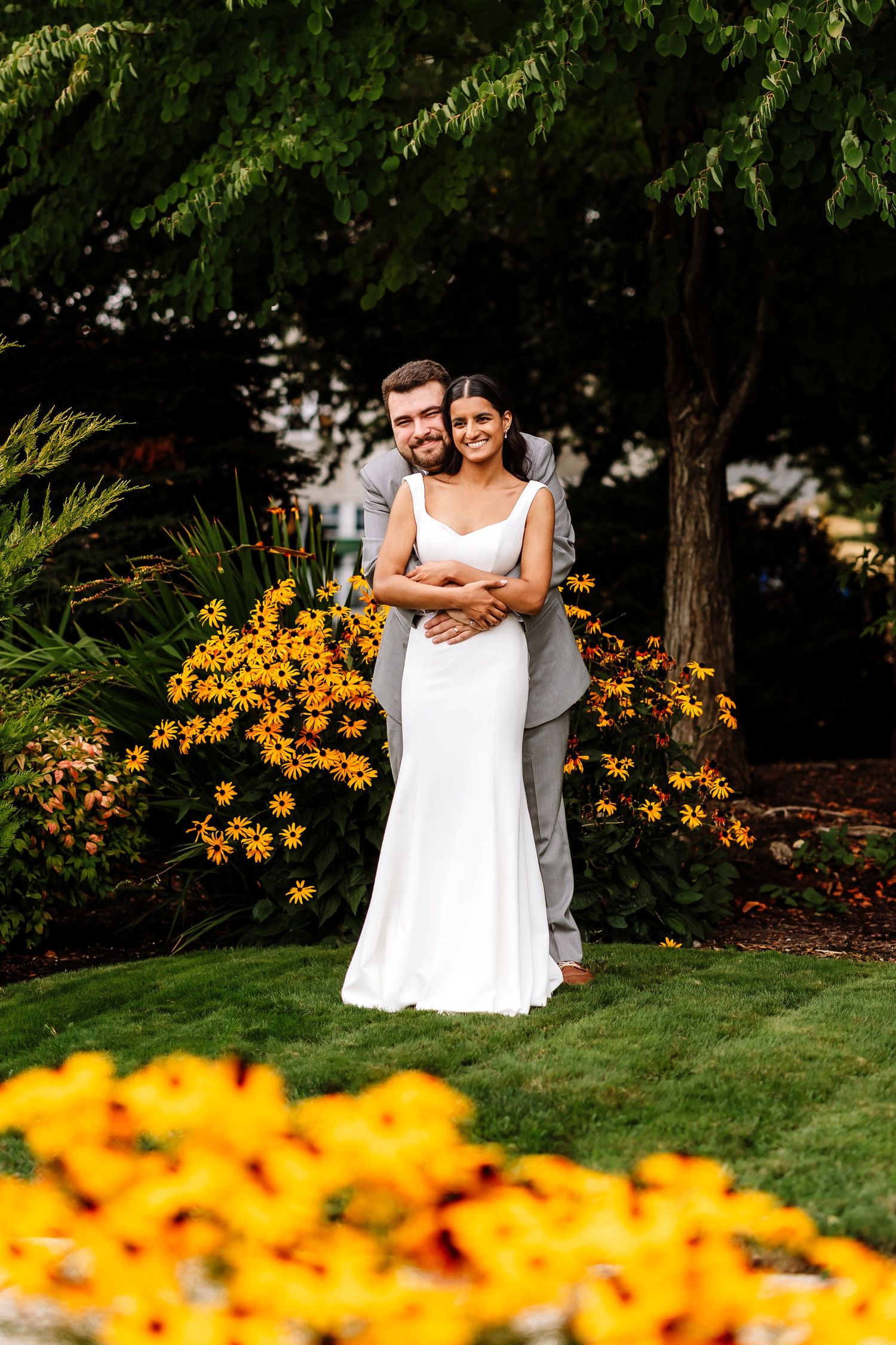 Bride and groom embracing in a lush garden surrounded by vibrant yellow black-eyed Susan flowers.