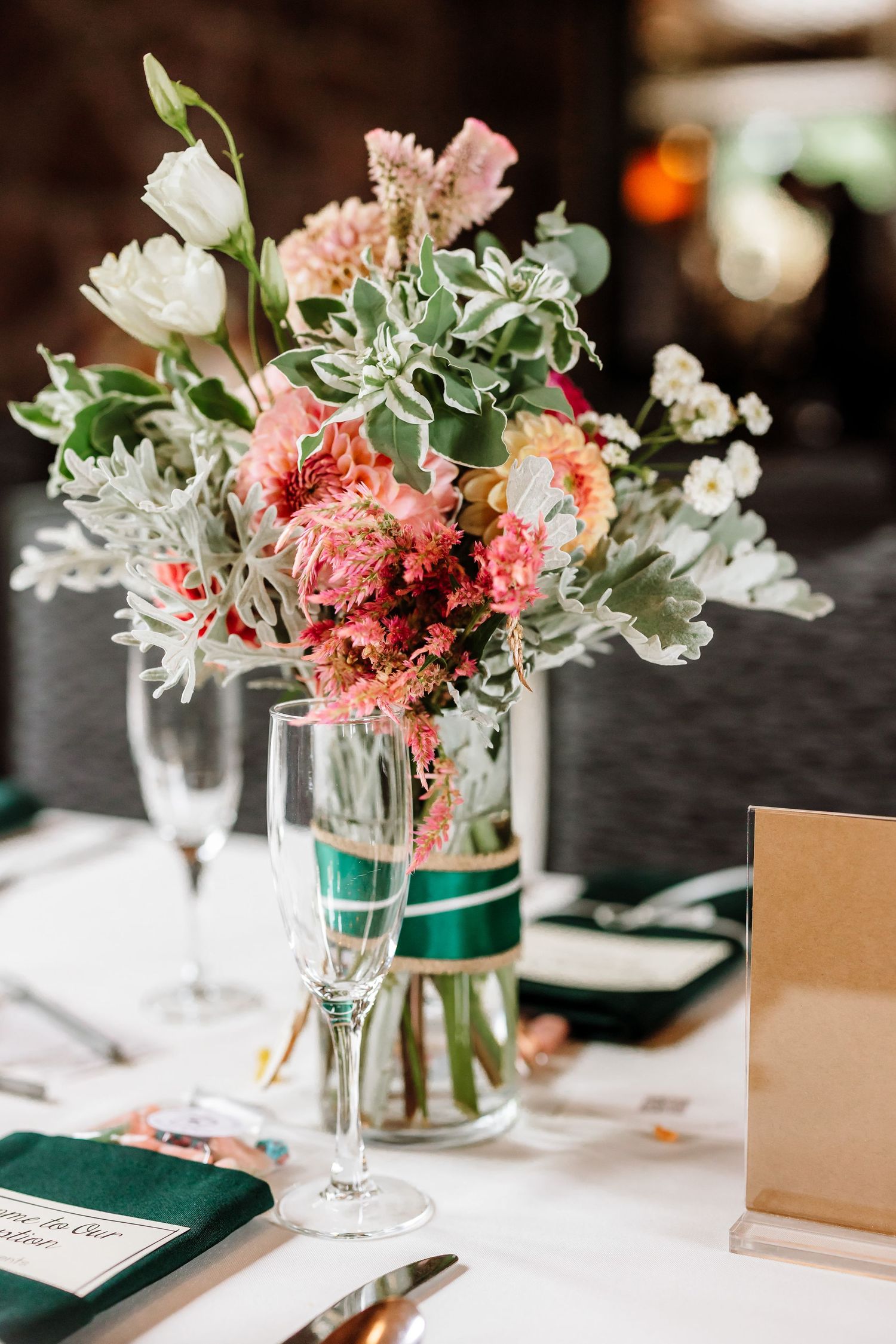 Pink and coral floral centerpiece with eucalyptus in a glass vase on a white wedding reception table.
