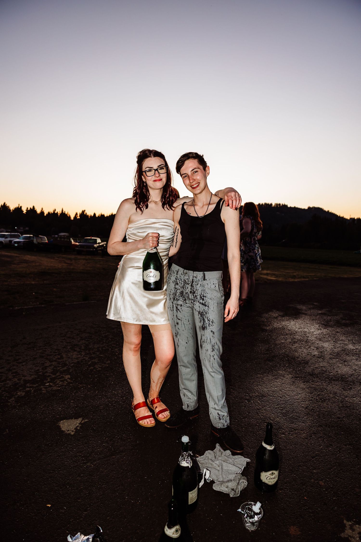 Couple posing at sunset holding champagne bottle at outdoor wedding celebration.