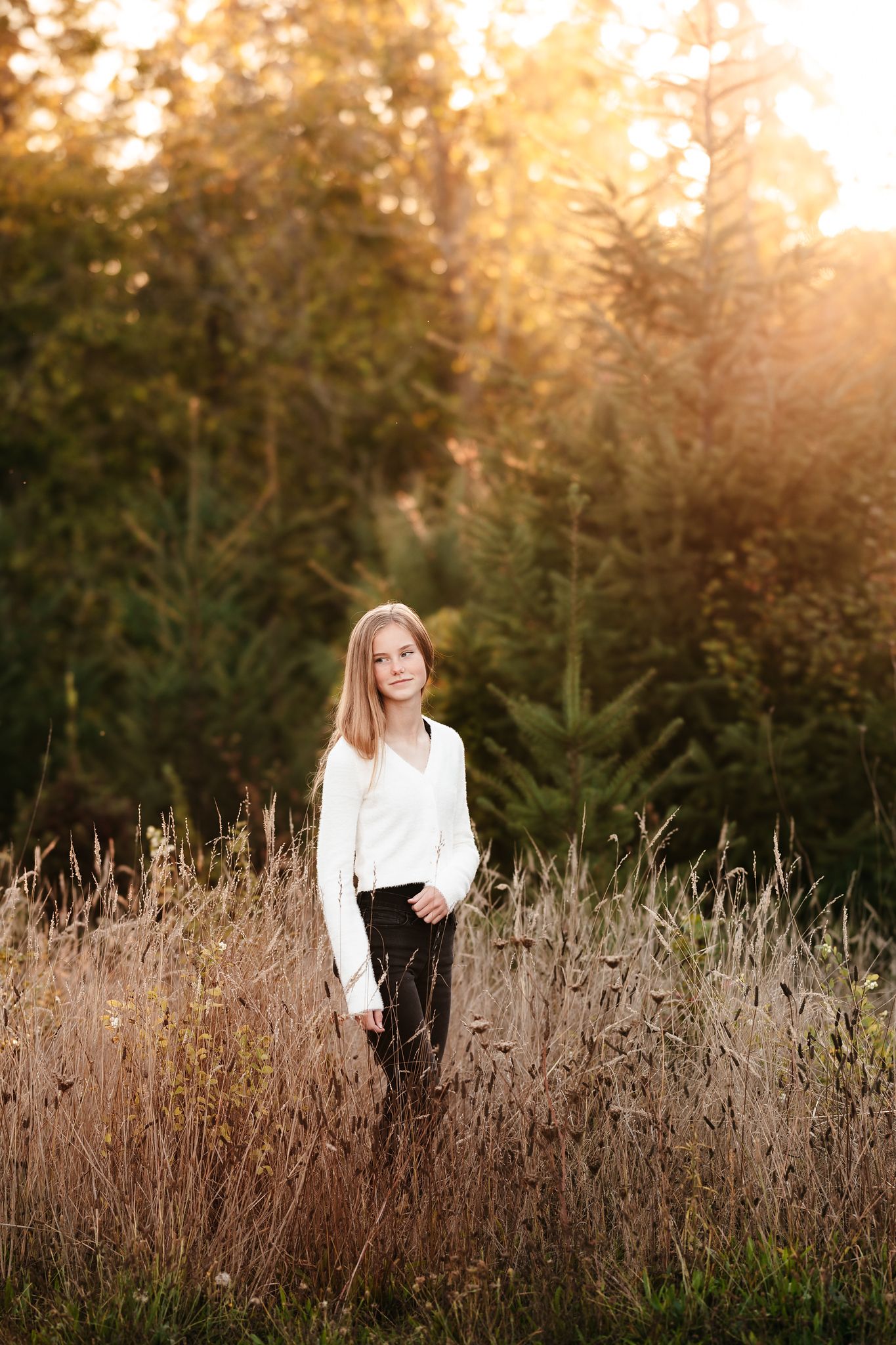 Young girl in white top and black pants standing in golden hour meadow.