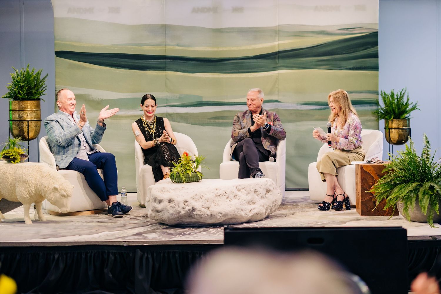 Four panelists engaged in lively discussion on stage with nature-inspired backdrop and decorative plants.
