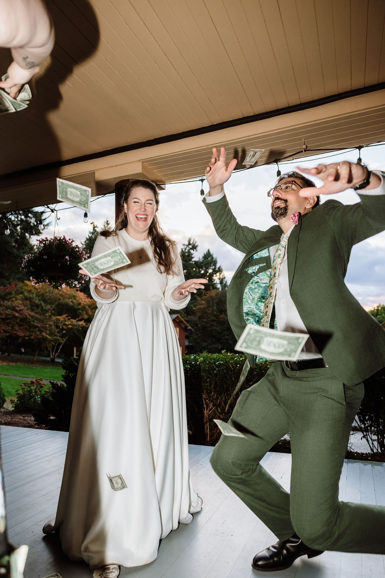 Joyful bride and groom tossing dollar bills in the air during a fun outdoor wedding celebration.