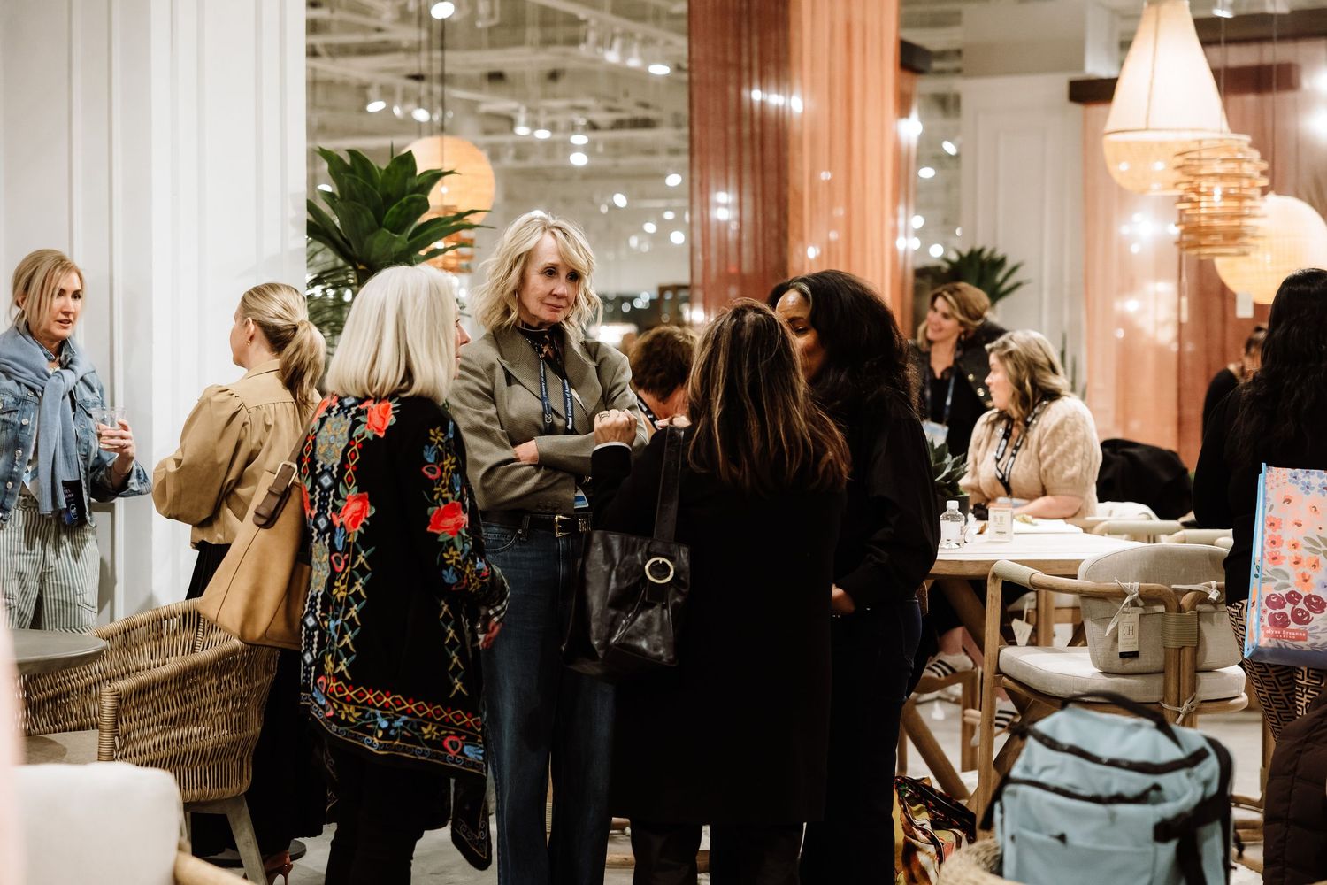 Women network and mingle in a warmly lit furniture showroom at a trade event.