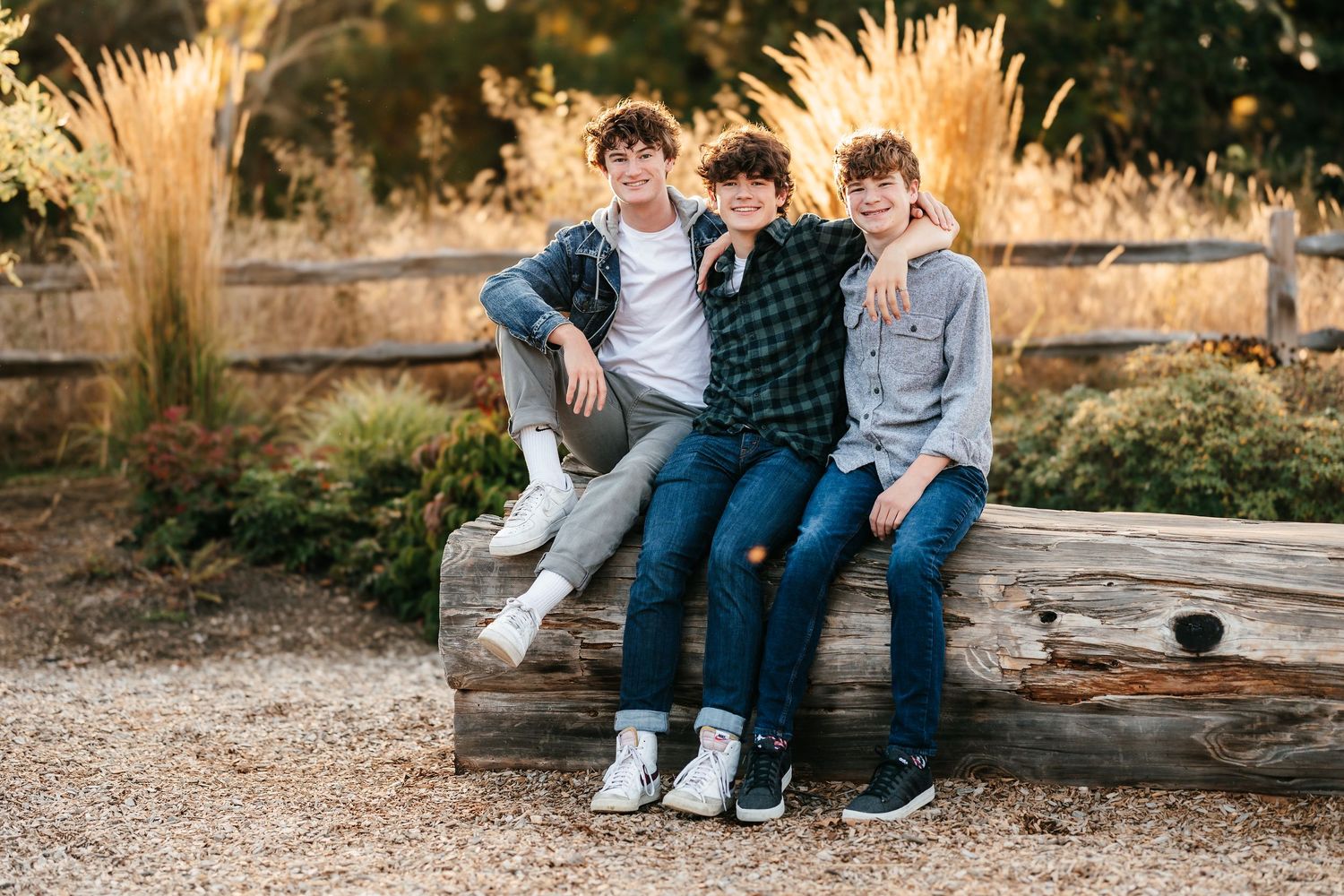 Three teenage boys sitting together on a rustic wooden bench outdoors, smiling and posing for a portrait photo.