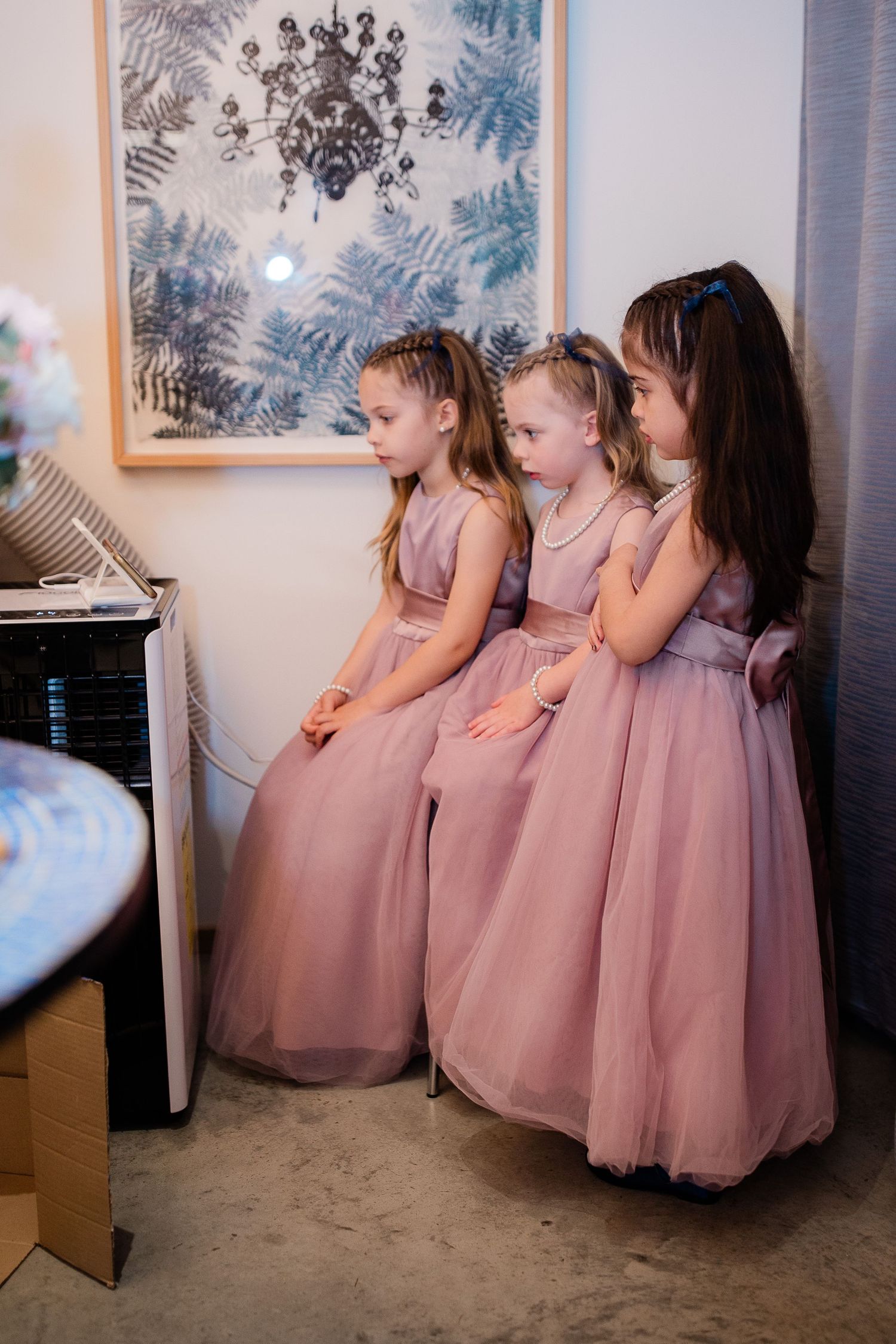 Three young flower girls in dusty rose tulle dresses stand together before the wedding ceremony.