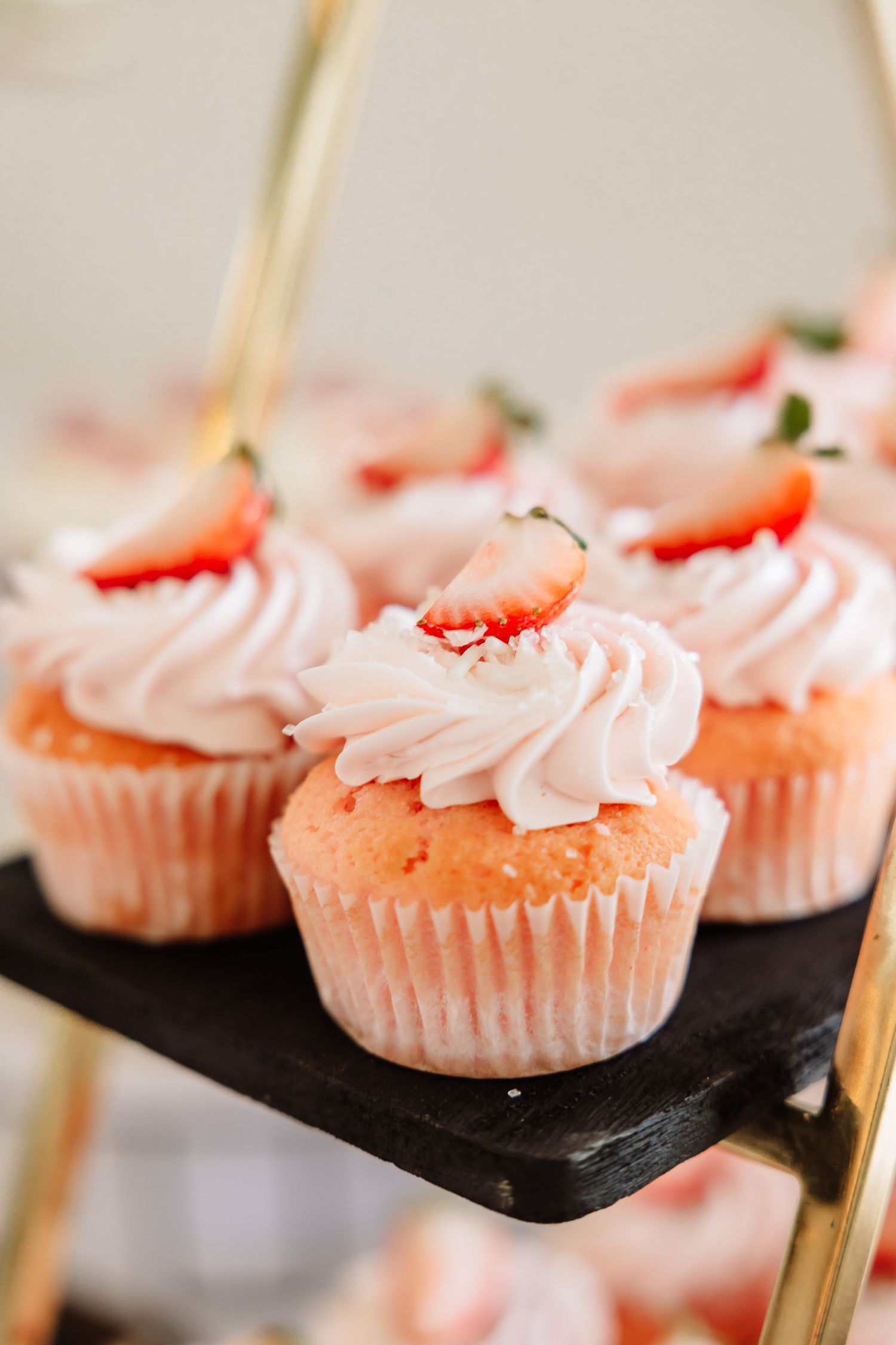 Pink strawberry cupcakes with white frosting and fresh strawberry slices on tiered stand.
