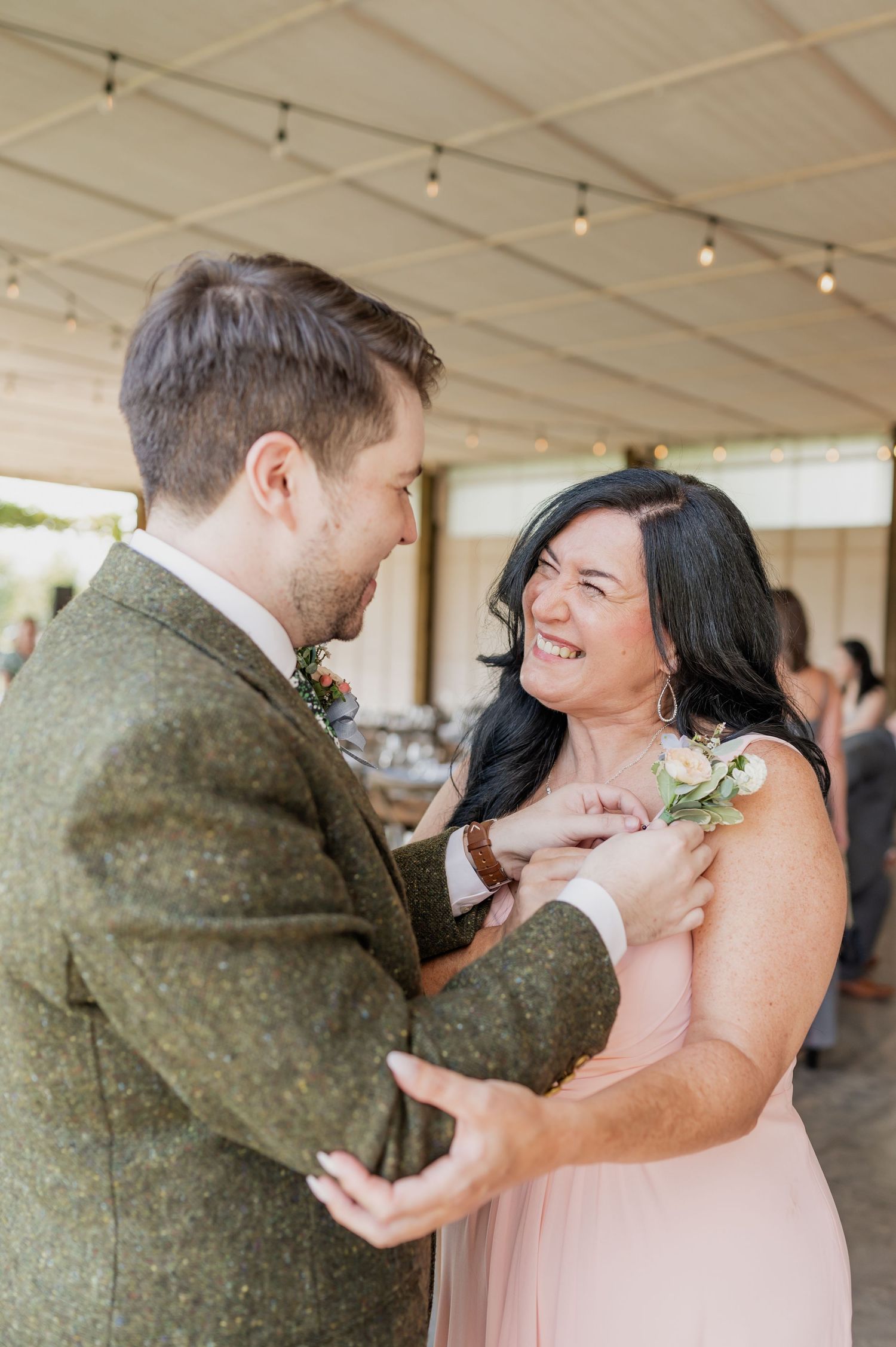 Groom in green tweed suit shares joyful dance with smiling woman in pink dress.