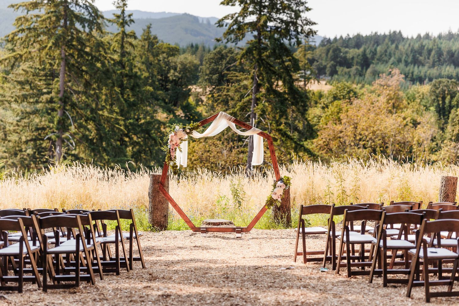 Rustic outdoor wedding ceremony setup with wooden arch, folding chairs, and scenic mountain backdrop.