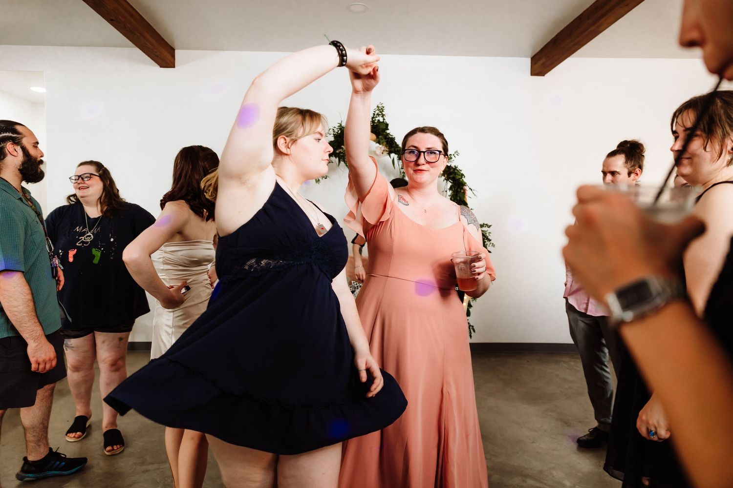 Two women in formal dresses dancing and holding hands at a wedding reception party.