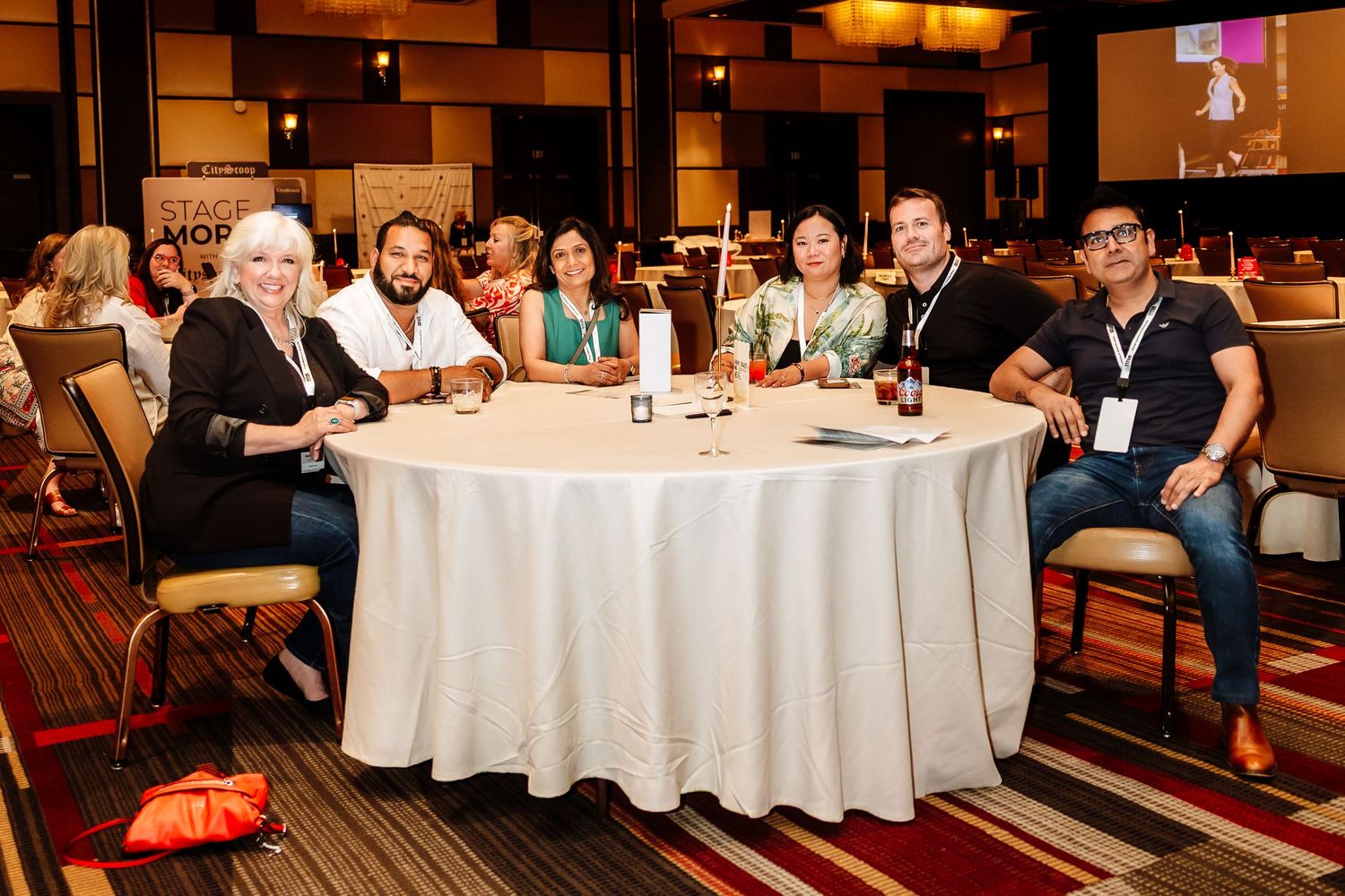 Seven conference attendees smiling at a round table during a professional networking luncheon event.