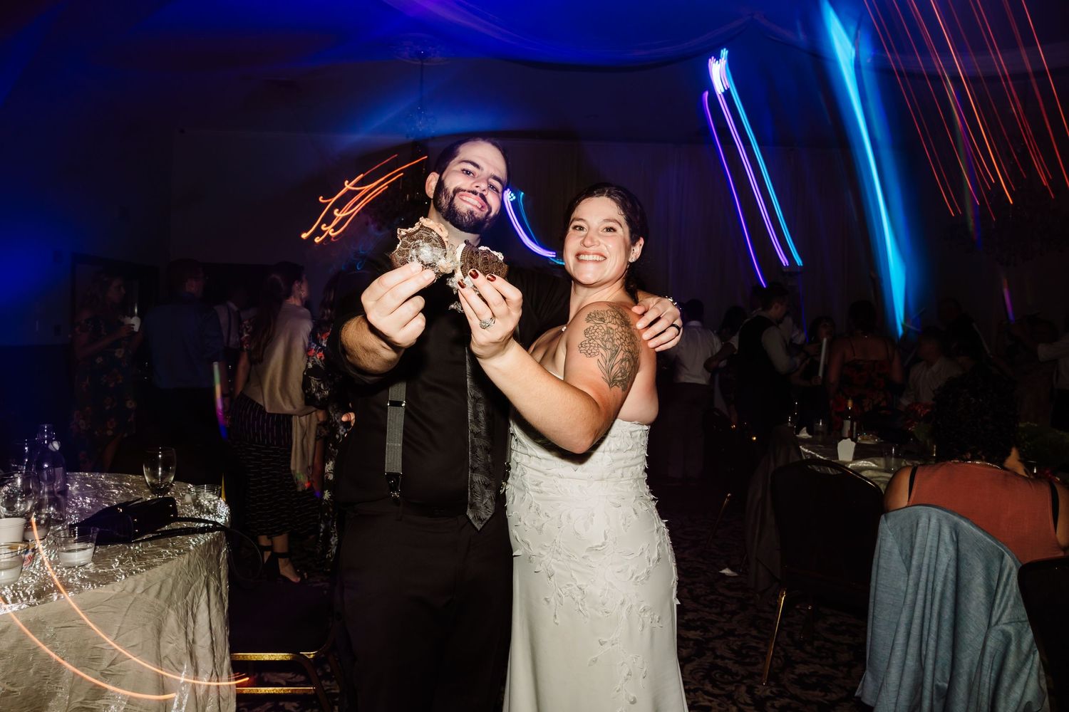 Bride and groom smiling and holding drinks at their wedding reception with colorful blue lighting.