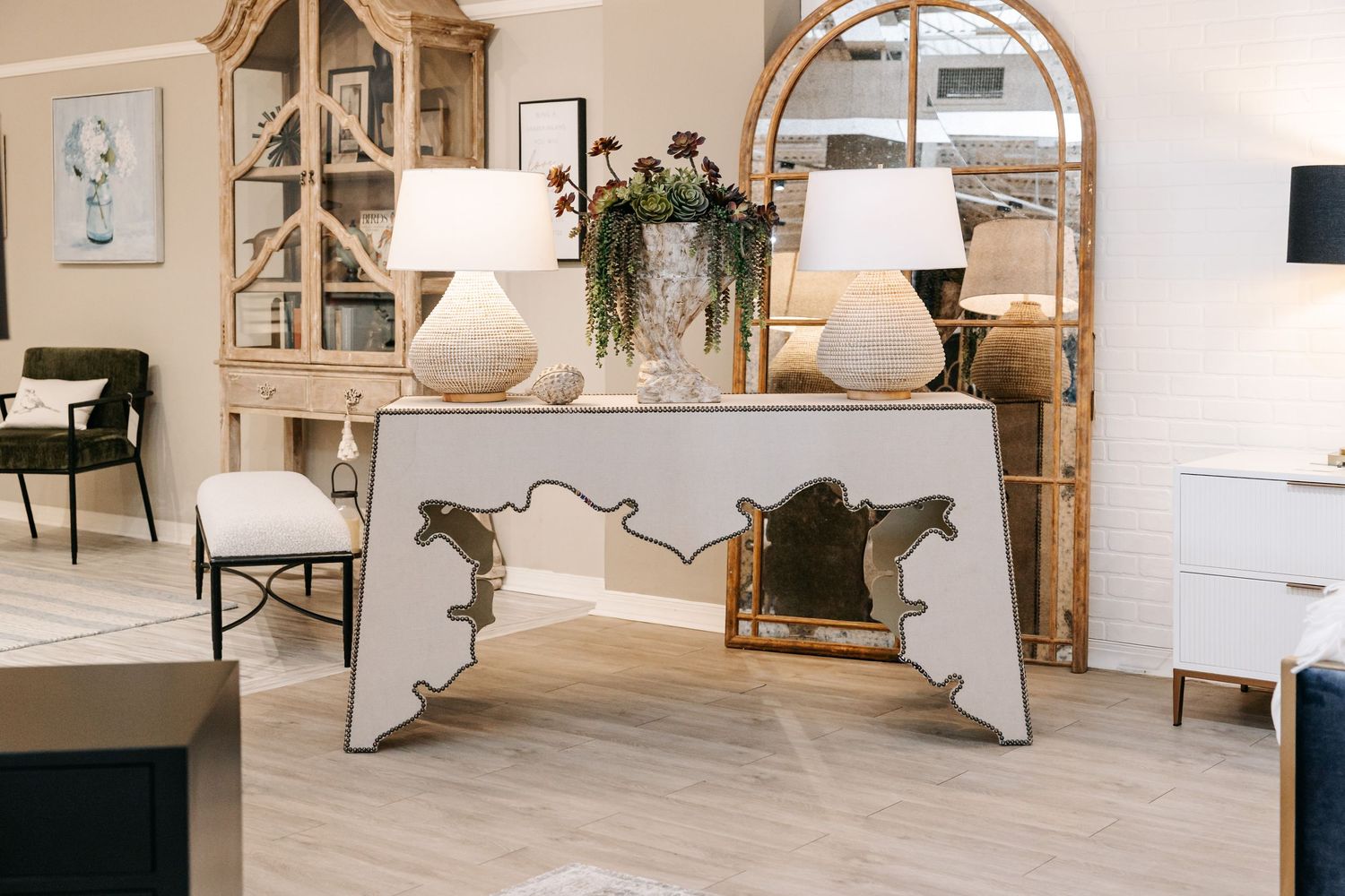 Bright interior design showroom with white console table, lamps, and arched mirror display.
