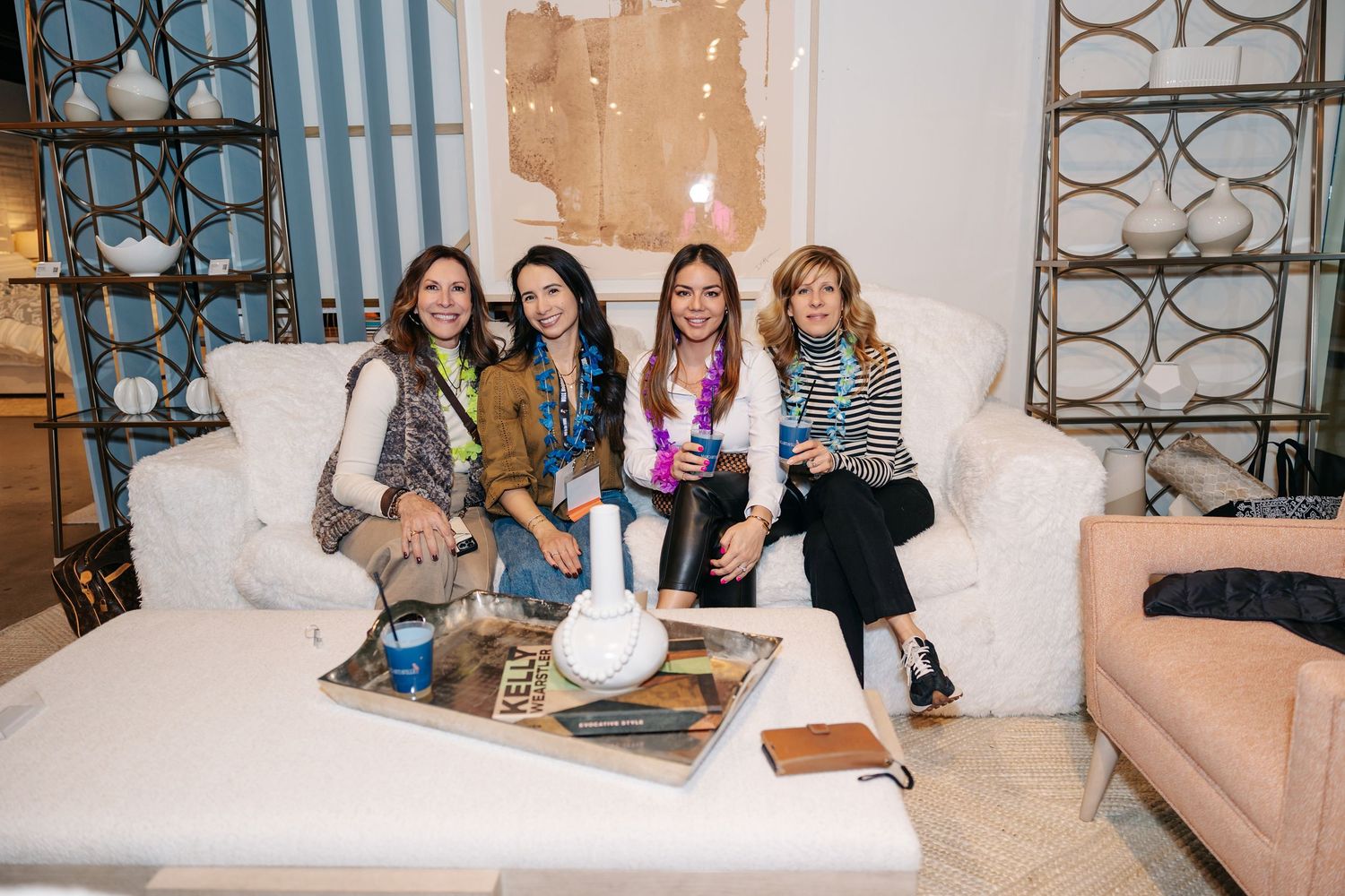 Four women smile together on a white sofa at an interior design showroom event.