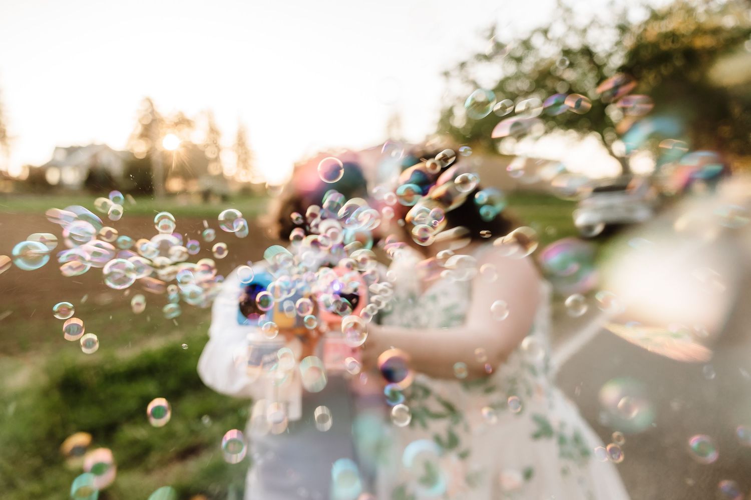 A couple blowing colorful soap bubbles together outdoors during golden hour at a wedding celebration.