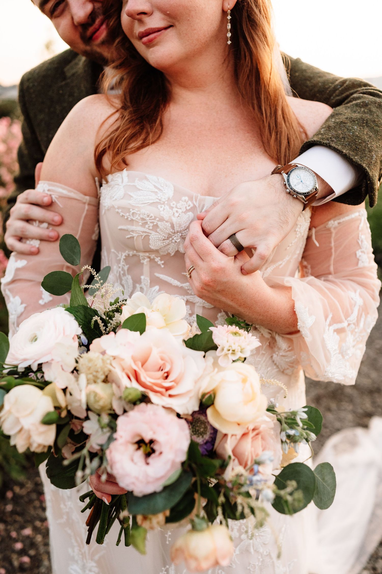 Close-up of groom embracing bride while she holds a lush blush and white rose bouquet.