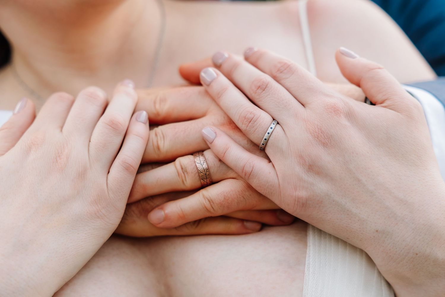 Close-up of bride and groom hands layered together showing wedding rings on wedding day.