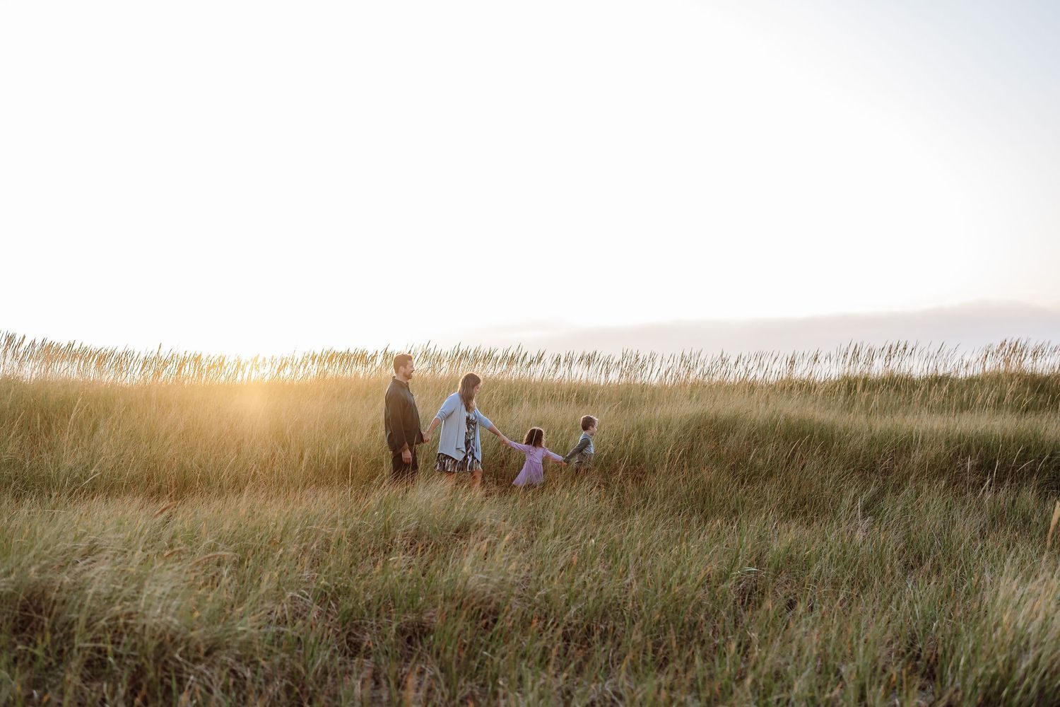 Family walking hand in hand through a golden grass field at sunset.
