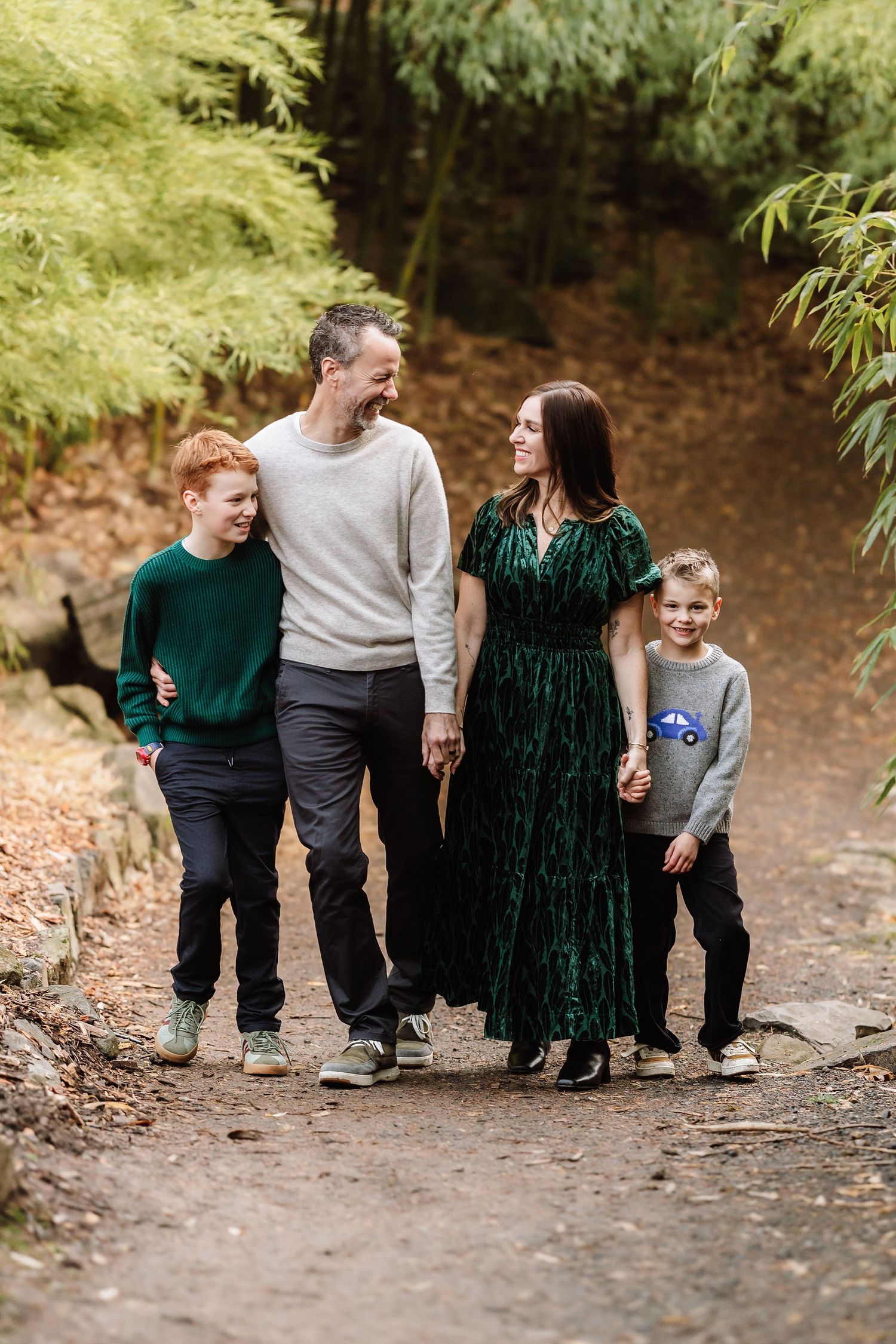 Family of four walking together on a forest path, smiling and laughing among lush green bamboo foliage.