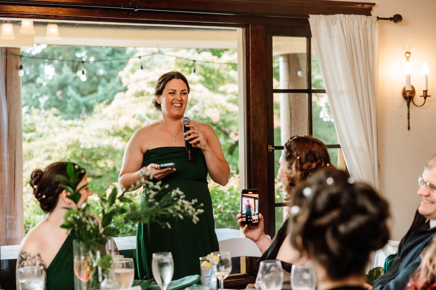 Bridesmaid in emerald green strapless gown delivers heartfelt speech at wedding reception.