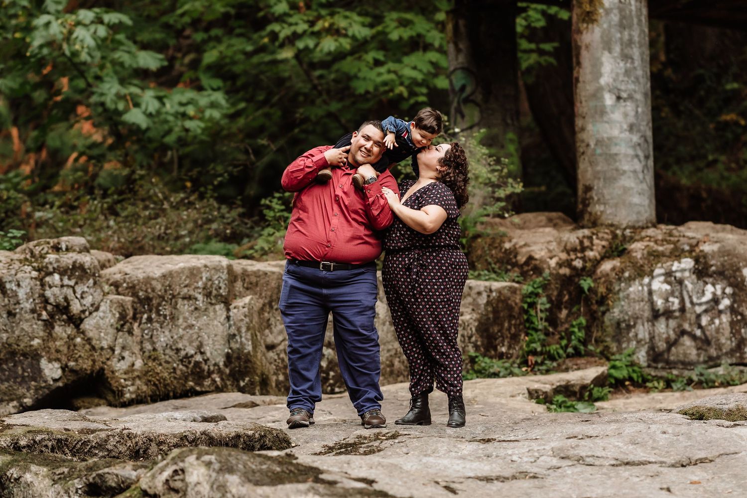Couple sharing a joyful moment together on rocky terrain surrounded by lush green forest.