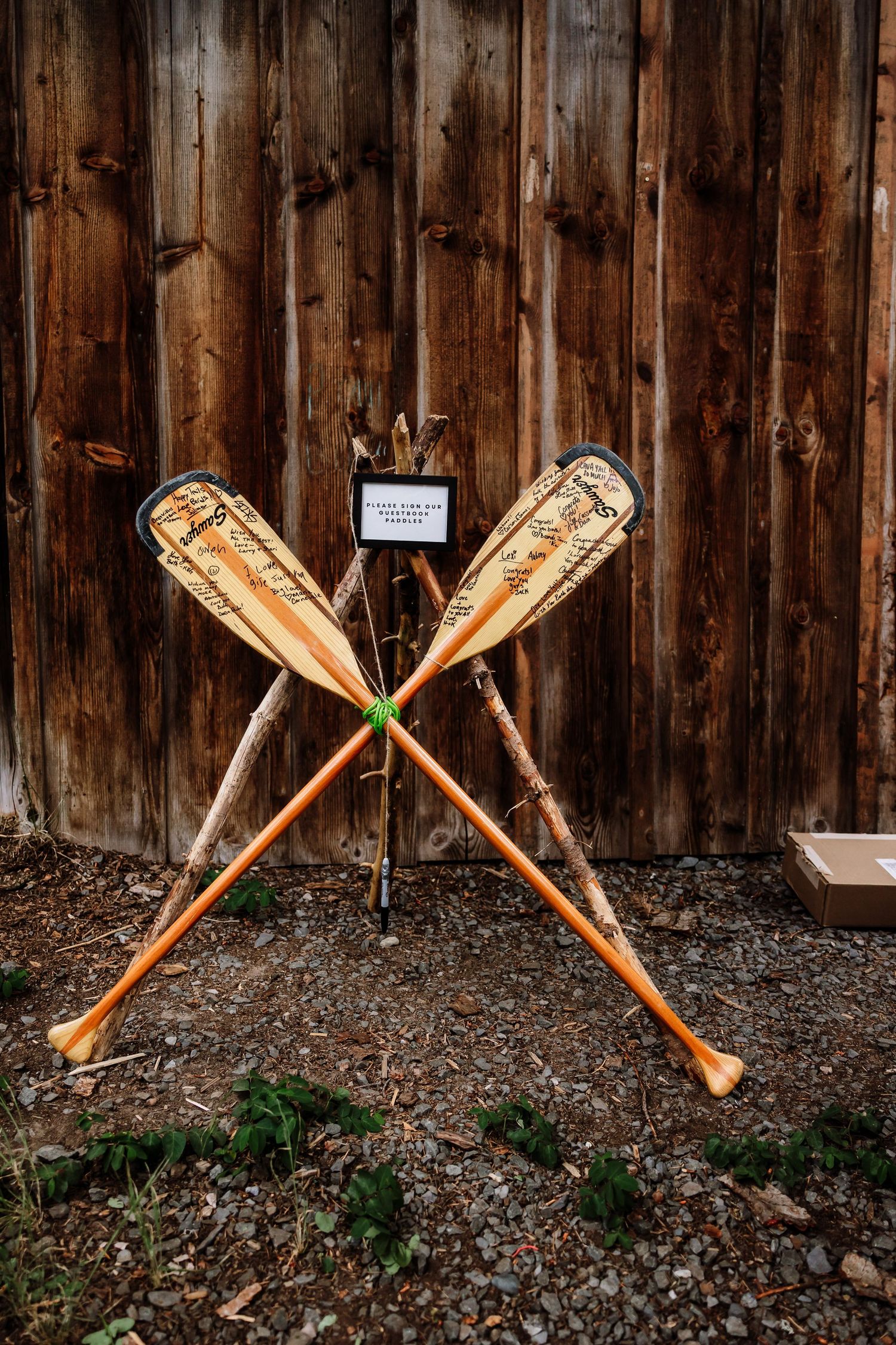 Decorated orange canoe paddles crossed against rustic wooden barn wall at outdoor wedding.