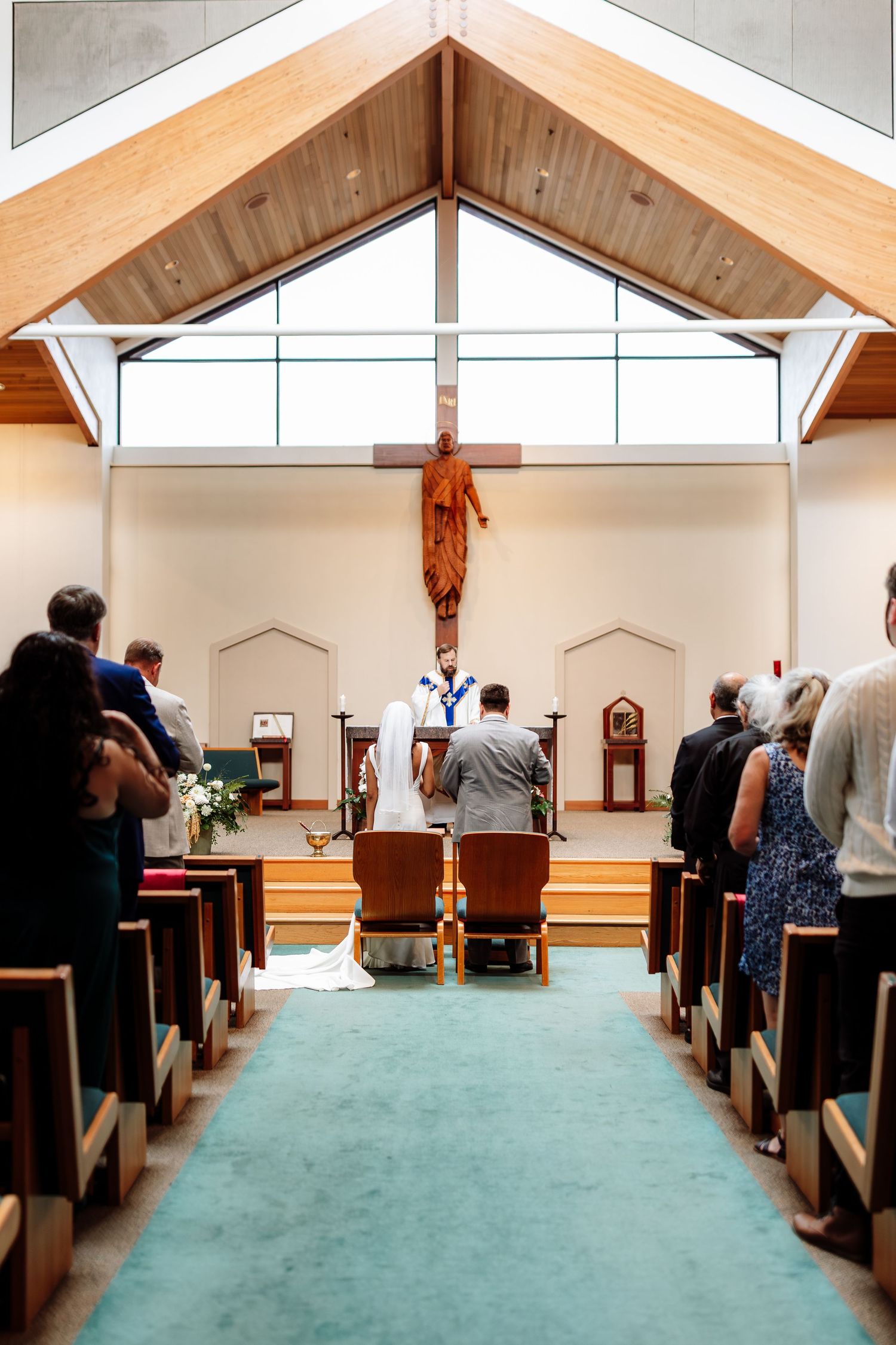 Bride and groom kneel at altar during wedding ceremony in modern church with wooden cross.