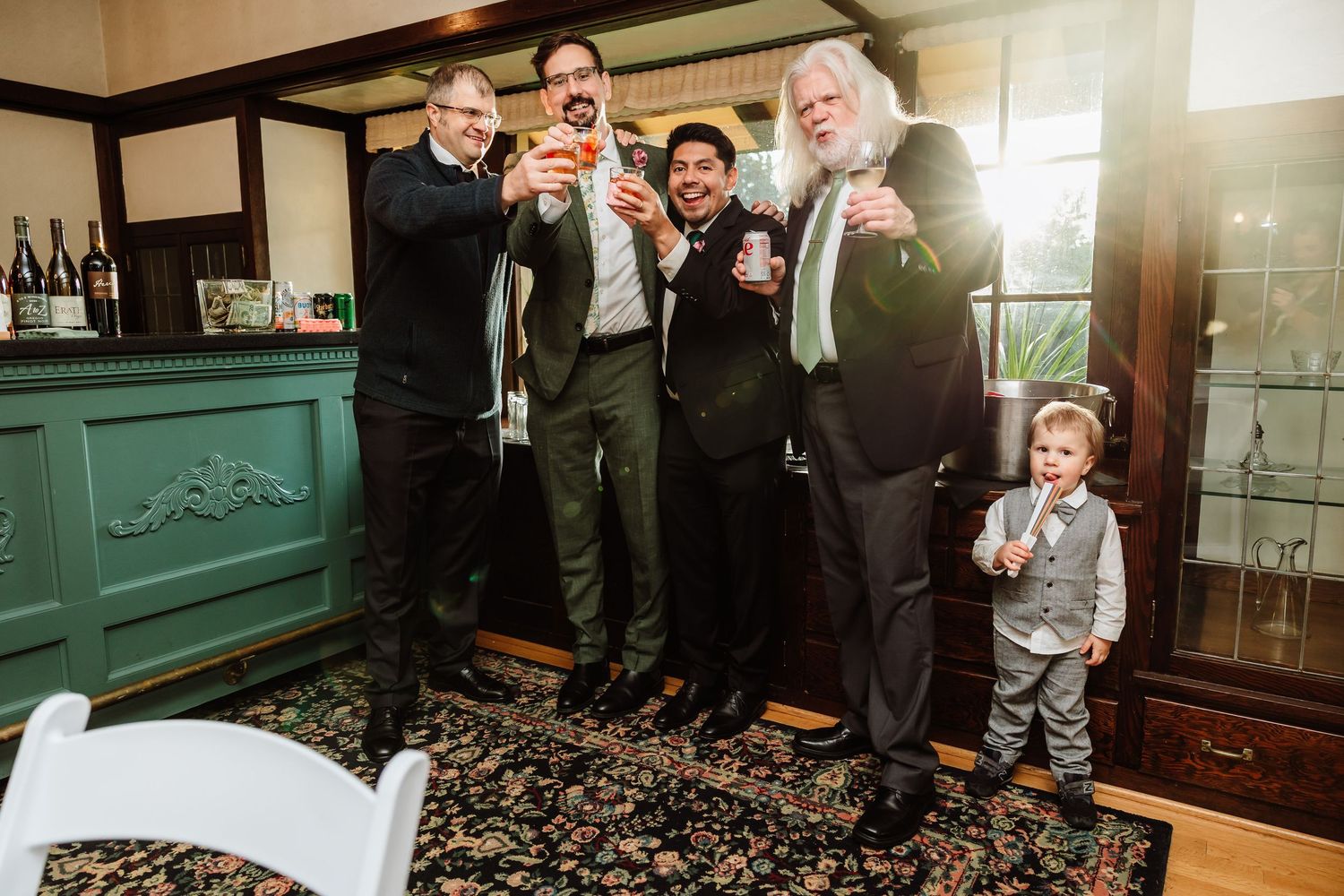 Four men and a small child in gray suit raise glasses for a toast at wedding reception.