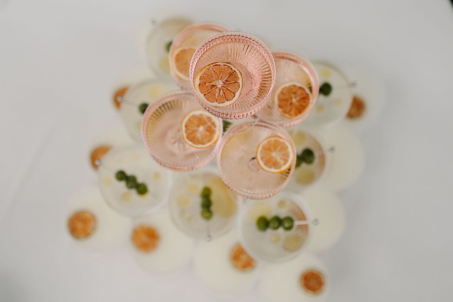 Overhead view of cocktail hour drinks garnished with dried citrus slices and green olives.
