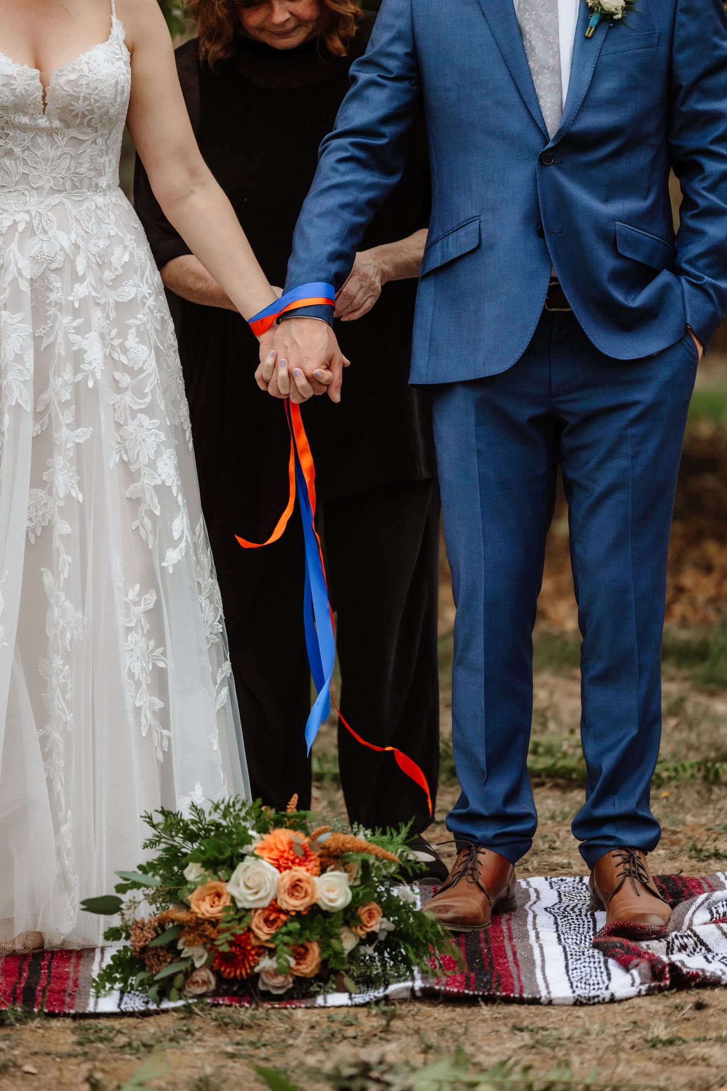 Close-up of bride and groom hand-fasting ritual with colorful ribbons during outdoor wedding ceremony.