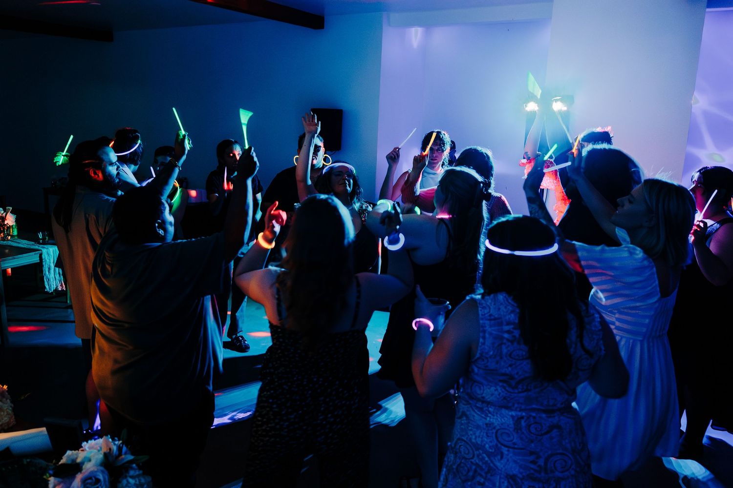 Wedding guests dancing with colorful glow sticks and neon bracelets at reception.