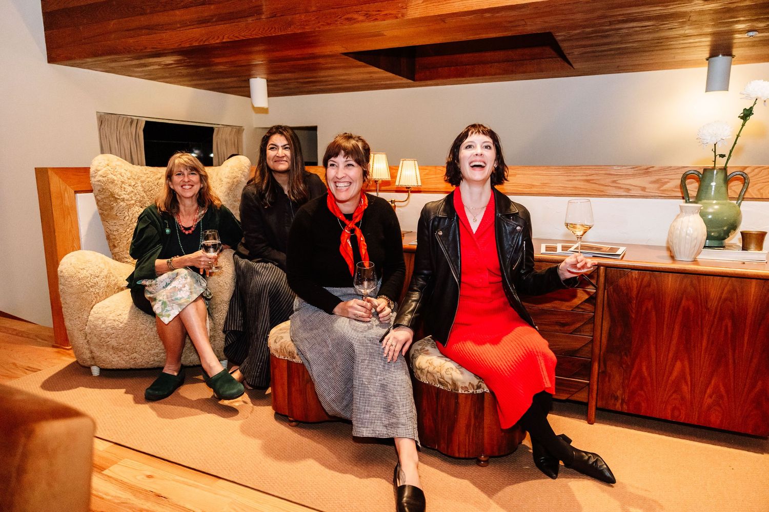 Four women laughing together seated on stylish furniture in a modern interior design space.