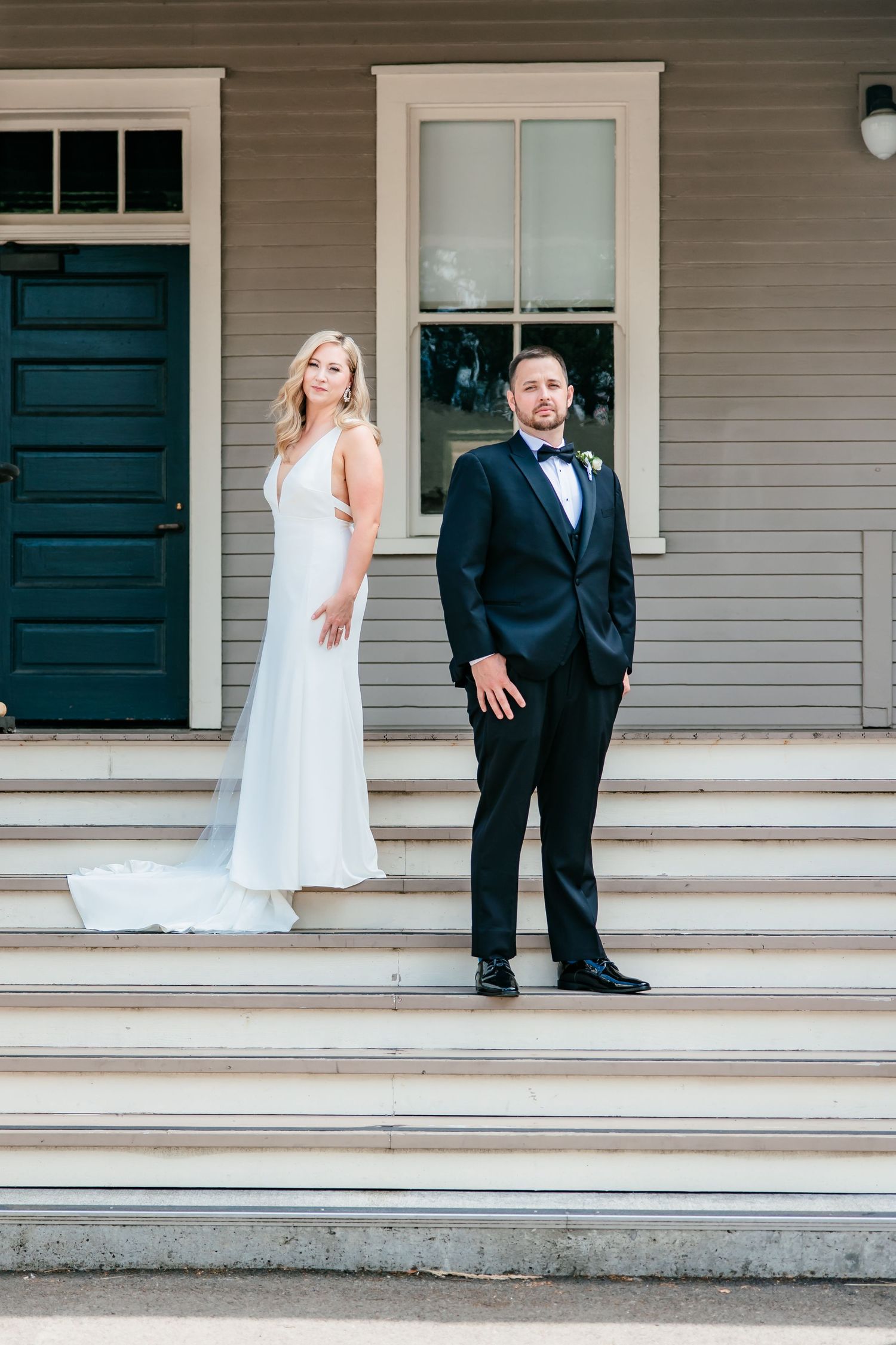 Elegant bride and groom posing on steps of a charming gray colonial wedding venue.