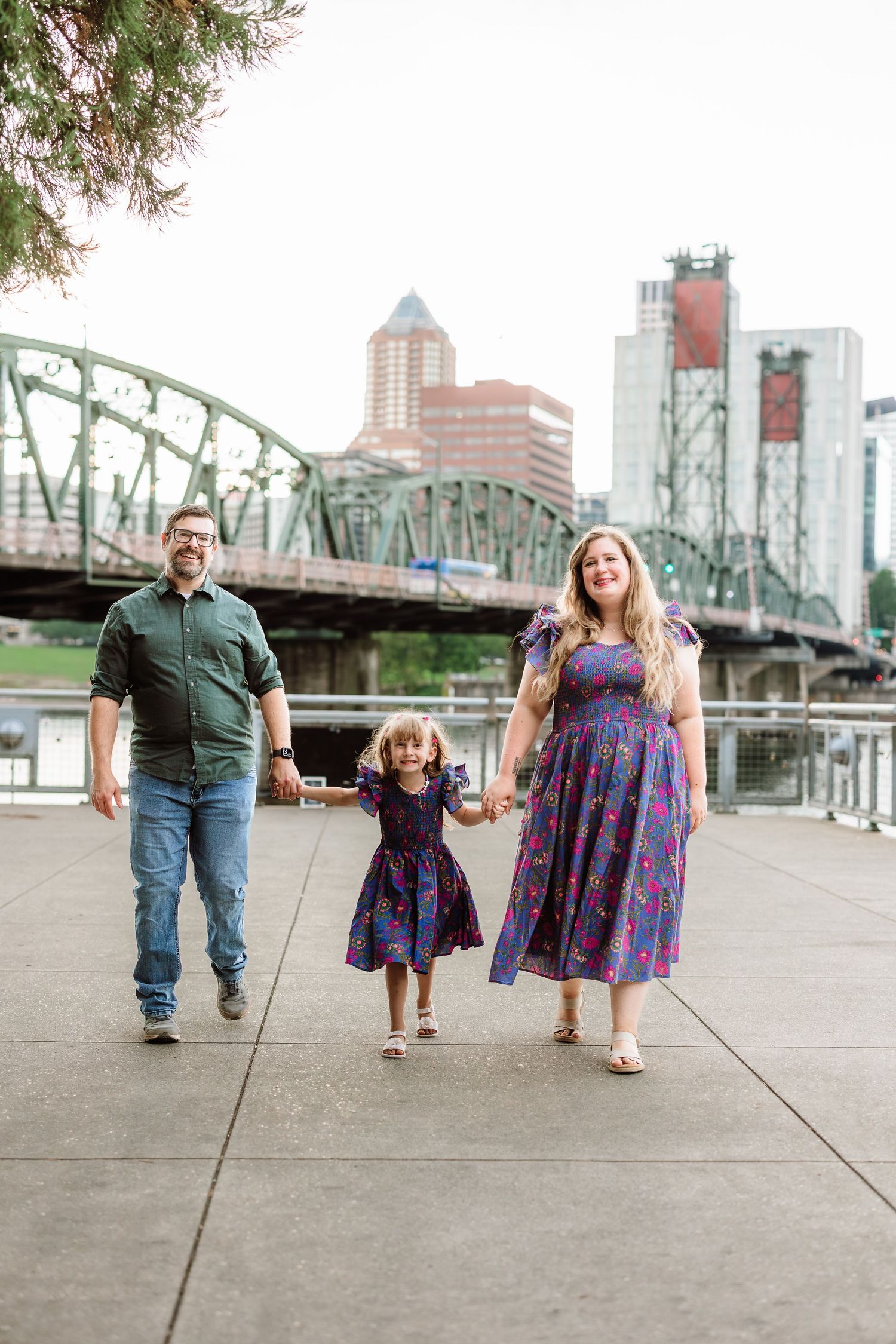 Family of three walking along Portland waterfront with Hawthorne Bridge and city skyline in background.