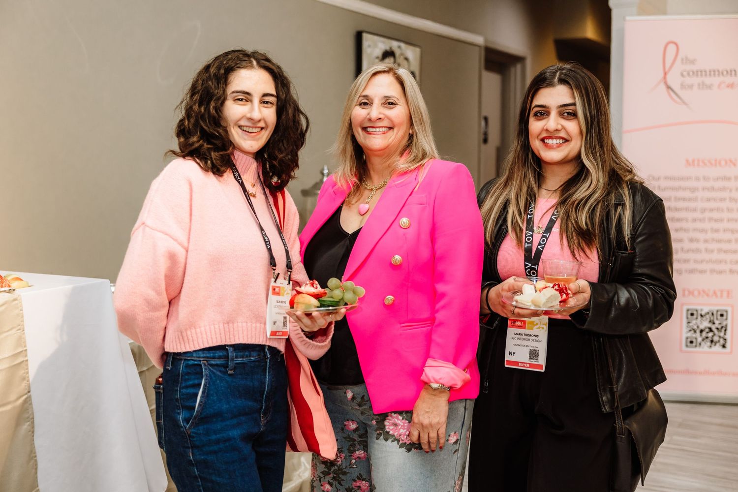 Three women smiling at a breast cancer awareness fundraising event wearing pink.