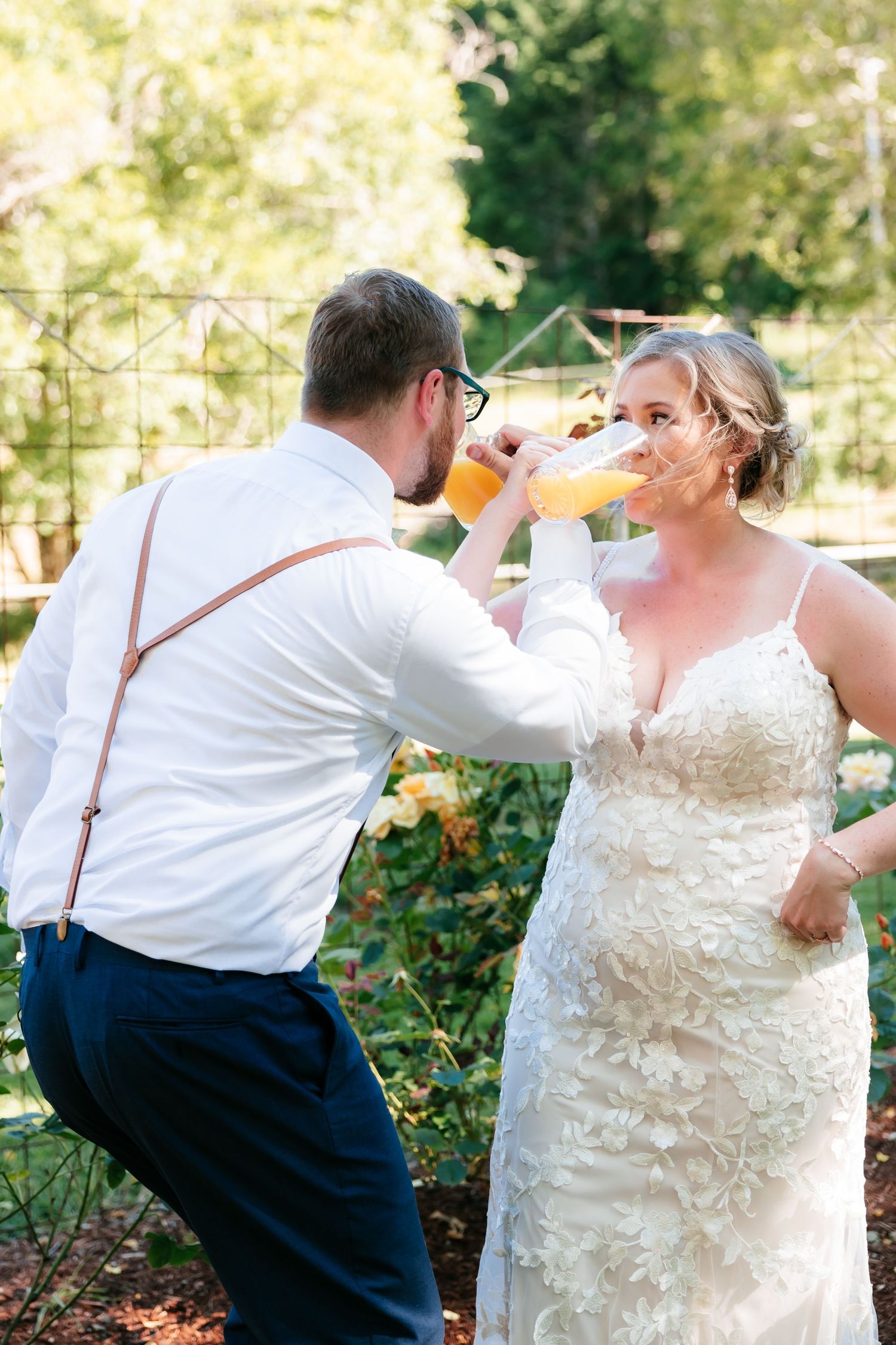 Bride and groom doing a crossarms champagne toast drink outdoors in a garden setting on their wedding day.