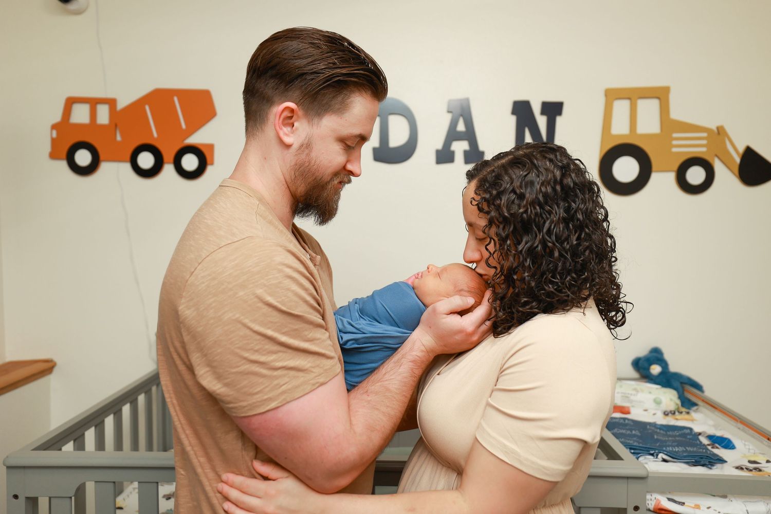 New parents sharing a tender moment together while holding their swaddled newborn baby.