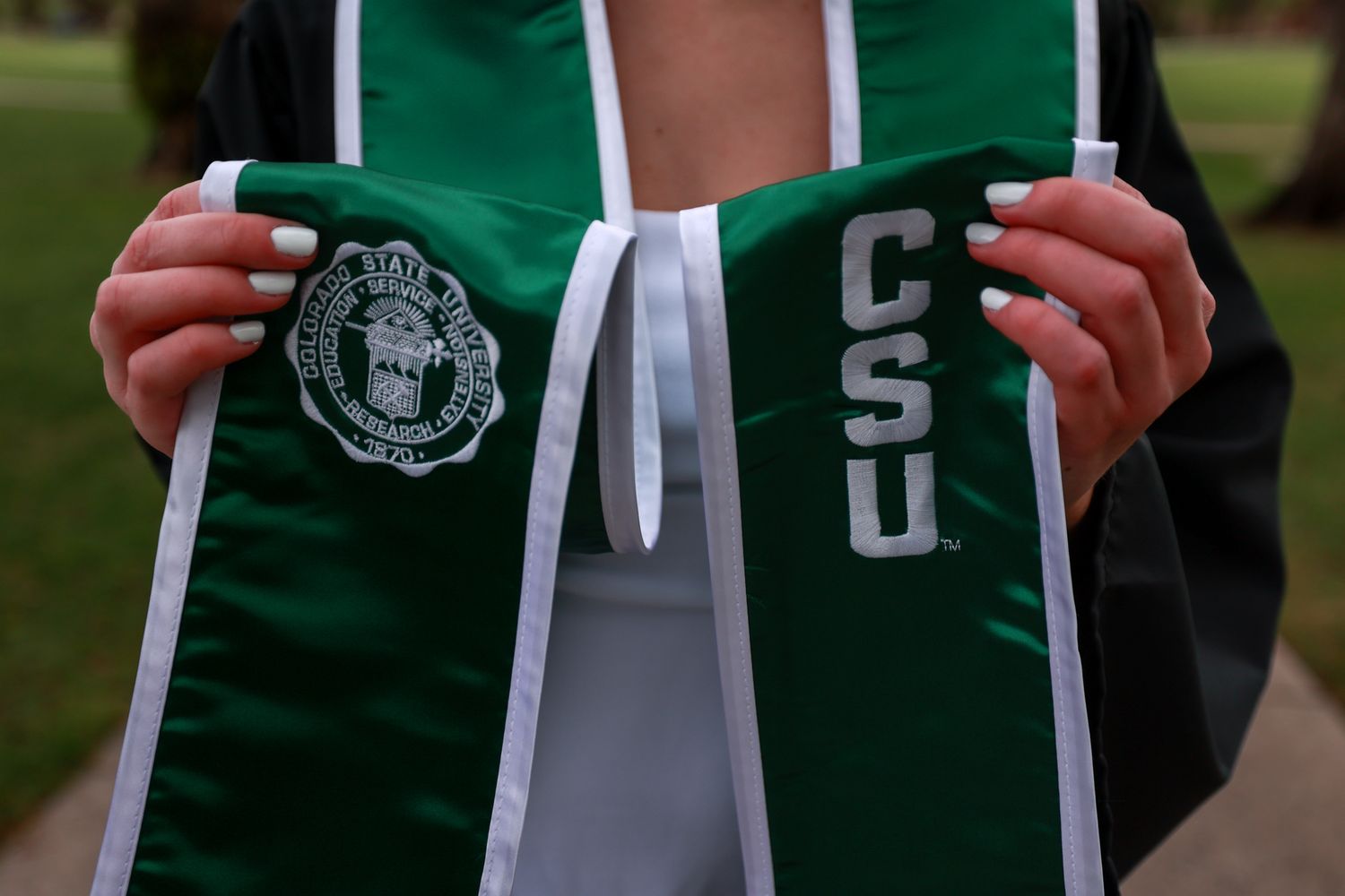 Person holding a green CSU graduation stole with white lettering and university seal.