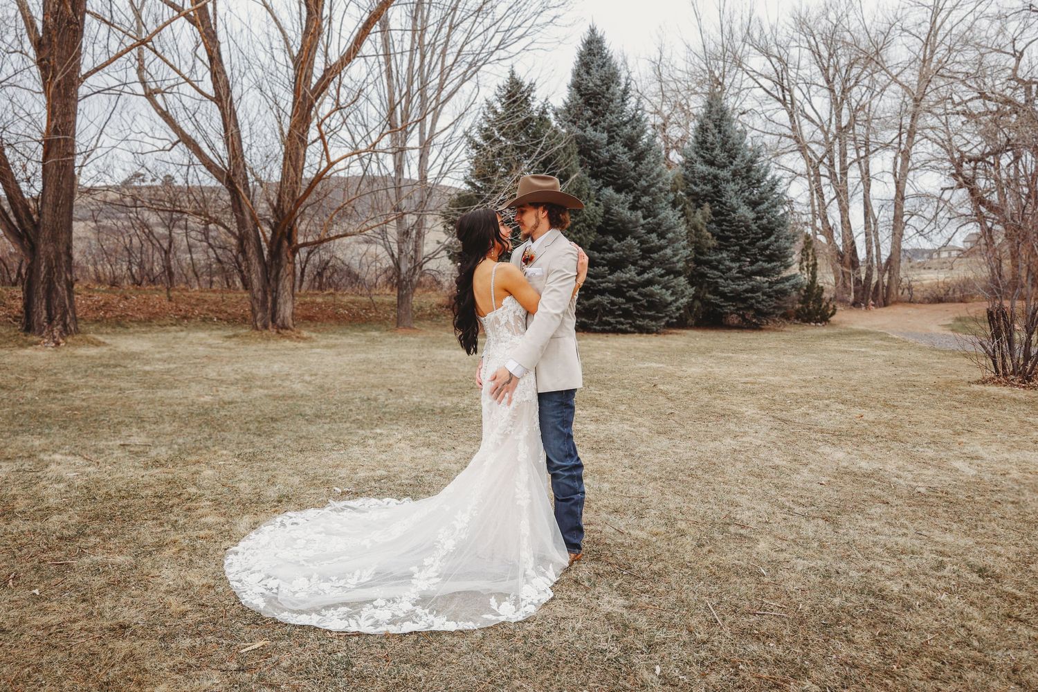 Bride and groom sharing a romantic embrace in a winter landscape with evergreen trees behind them.