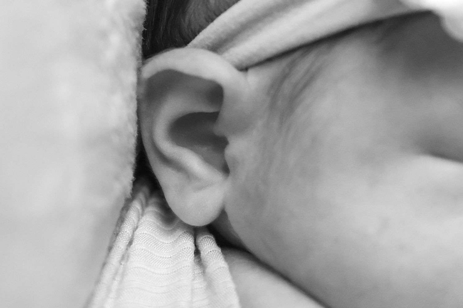 Close-up black and white photo of a newborn baby's ear resting on a soft white blanket.