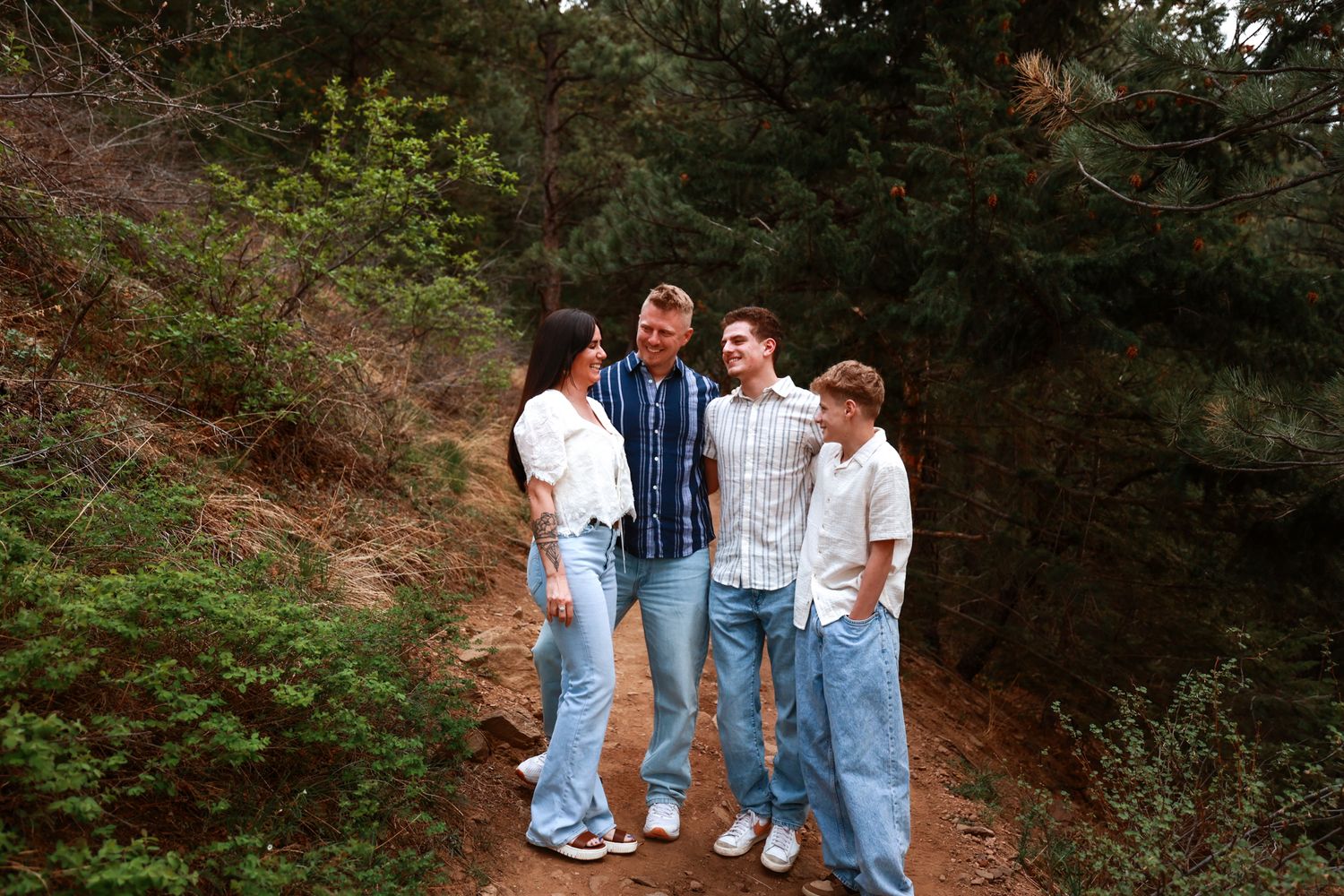 Family of four smiling together on a nature trail surrounded by lush green trees and rocky terrain.